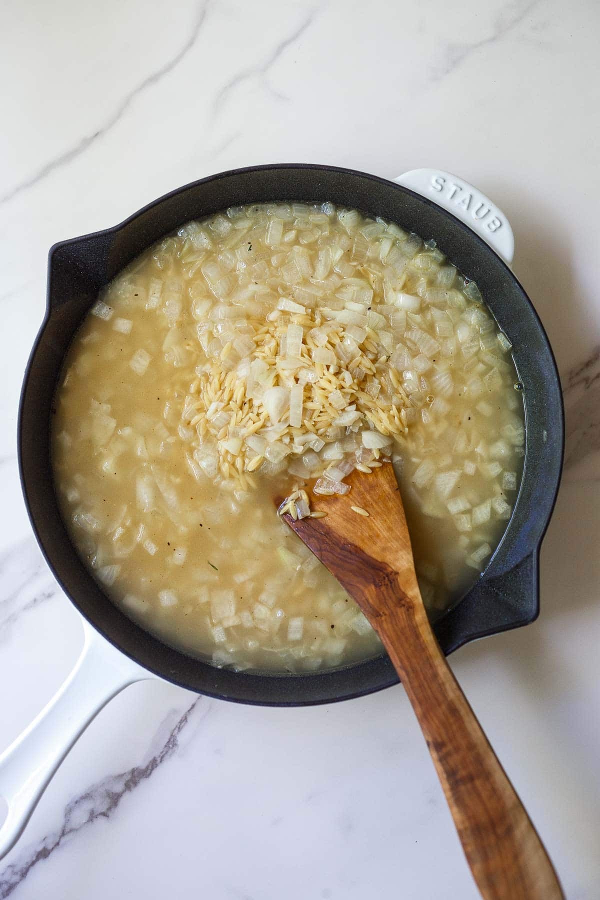 adding the broth to the skillet with a wood spoon to stir.