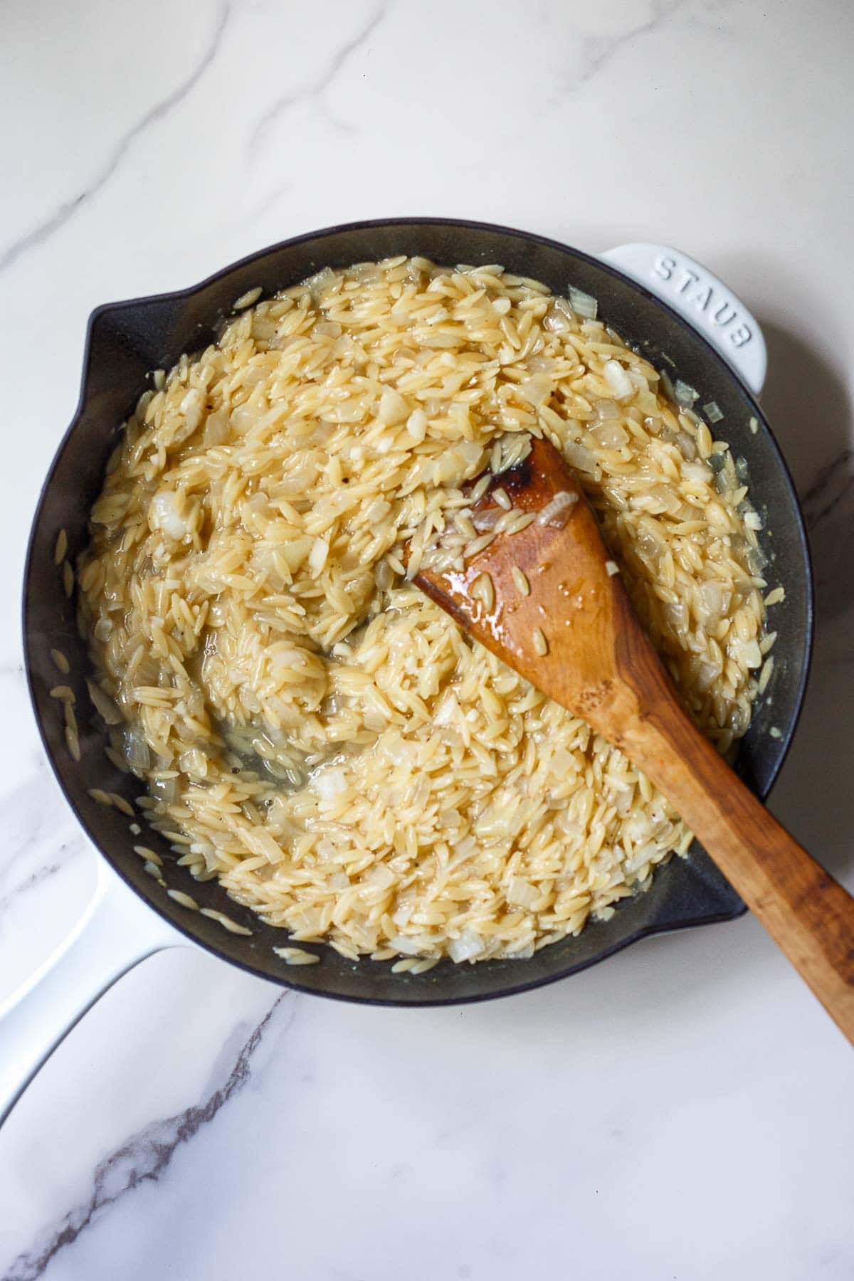 Making a Greek orzo skillet in one pan with creamy orzo and a wood spatula to stir.