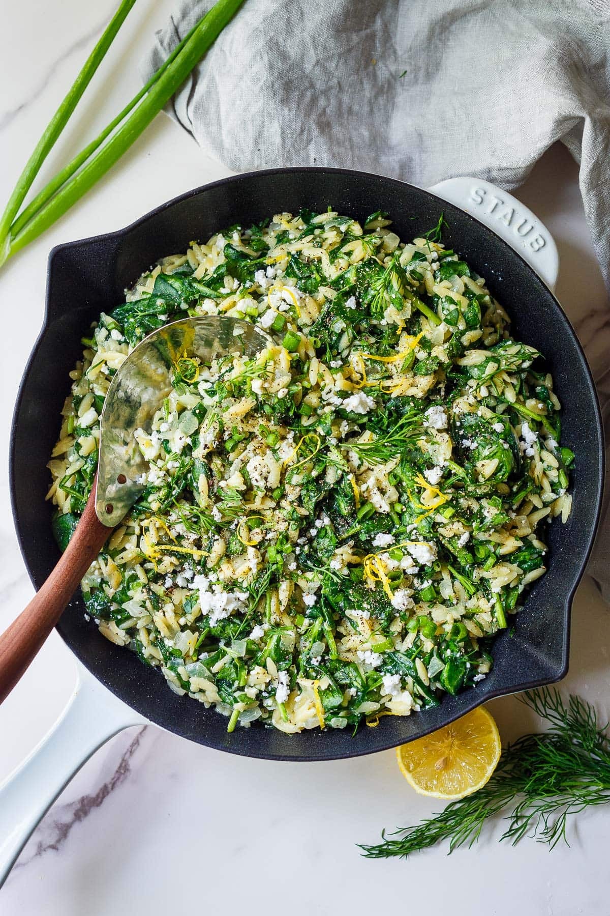 Greek Orzo Skillet with lemon zest, fresh dill, spinach, and feta, with a wood and metal spoon.