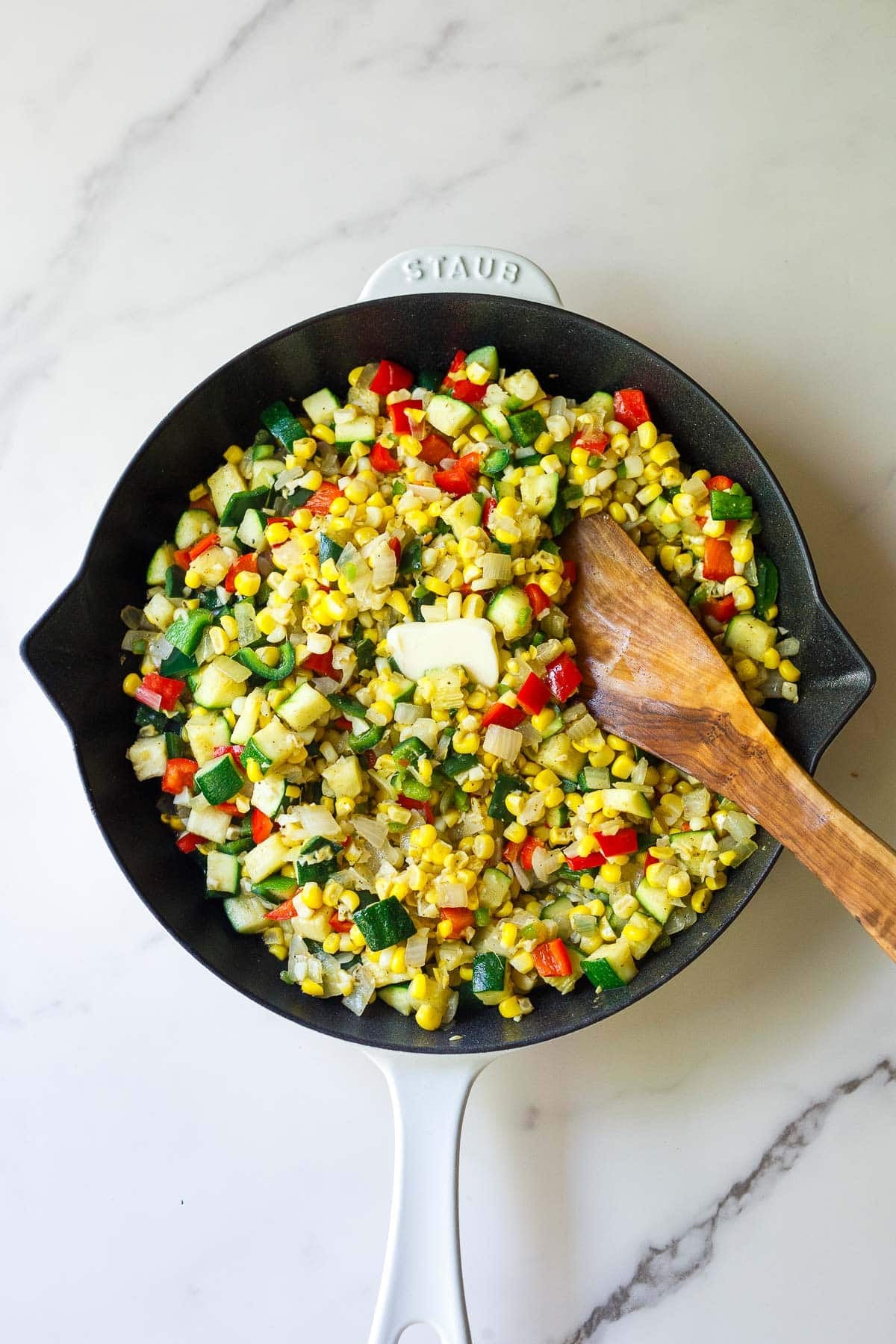 skillet with summer succotash cooking with a pat of butter and a wood spatula to stir.