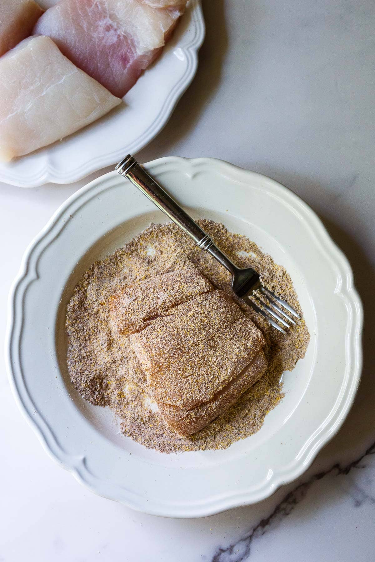 halibut fillet on a plate, dredged in cornmeal-flour mixture.