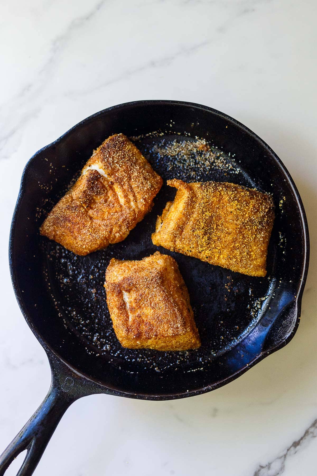 cornmeal crusted halibut searing in a cast iron skillet.