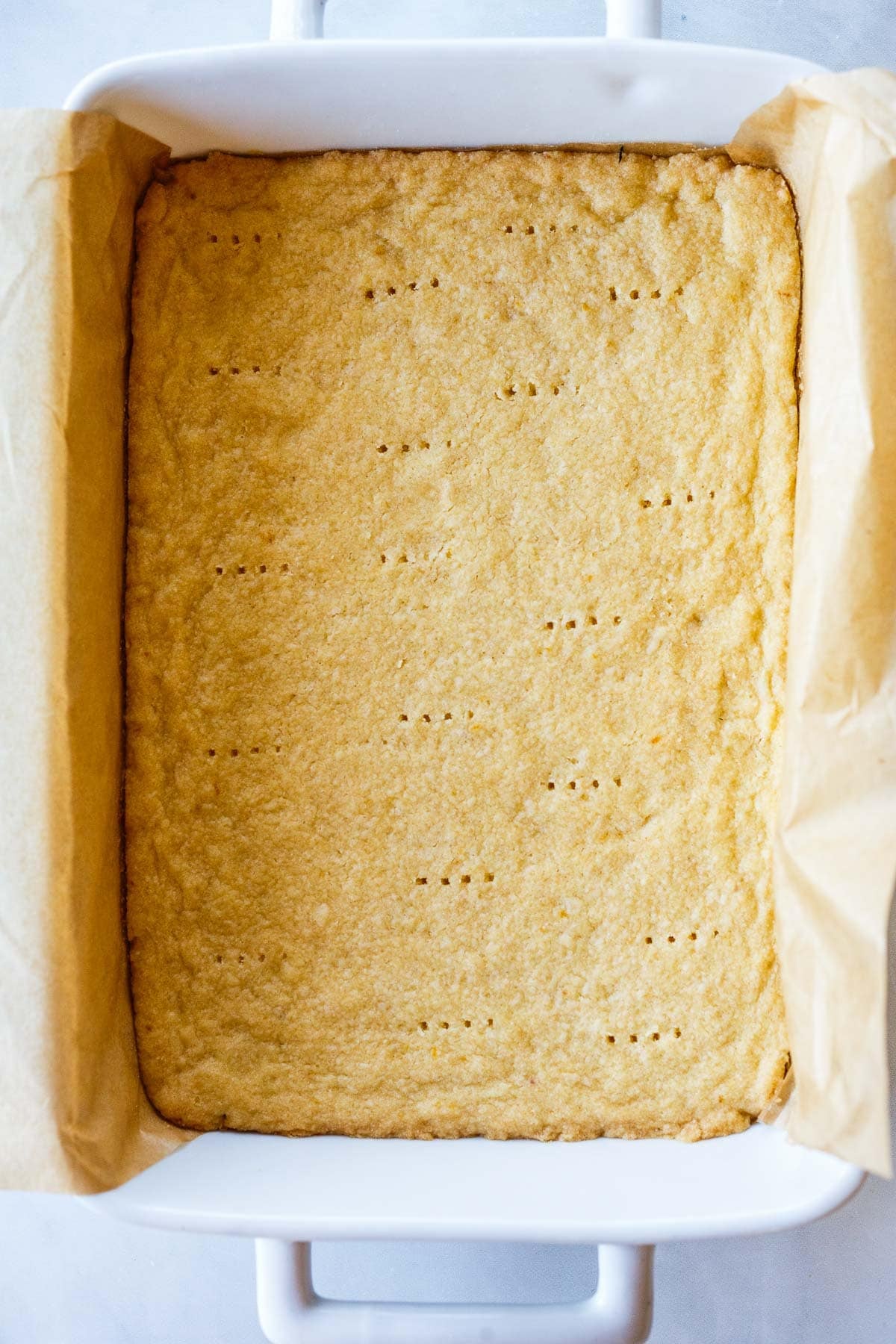 baked shortbread crust with fork pricks in a parchment-lined pan to make lemon bars.