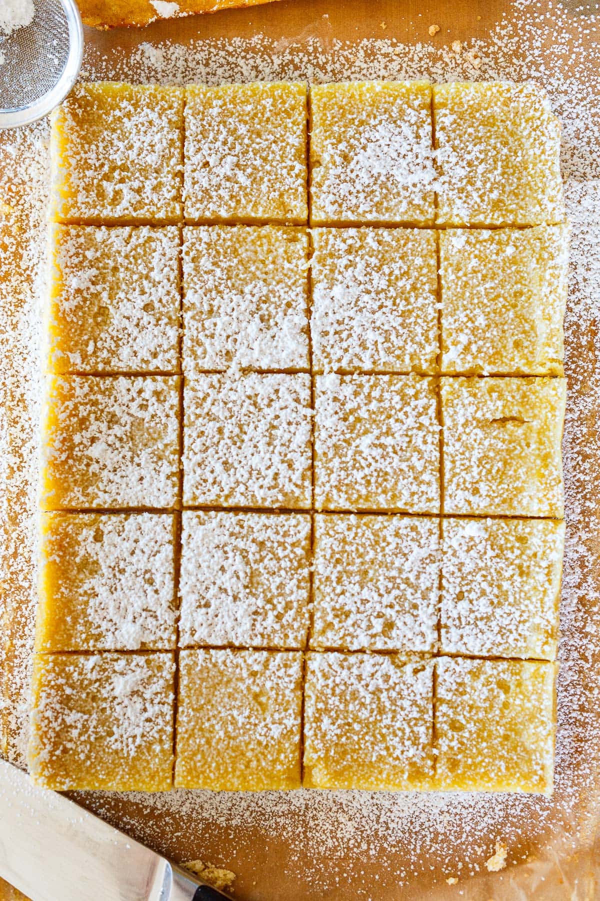 lemon bars cut into squares with powdered sugar on parchment paper.