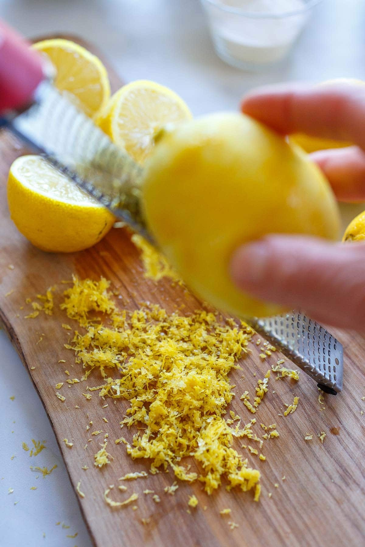 hand zesting a lemon onto a wood cutting board for lemon bars.