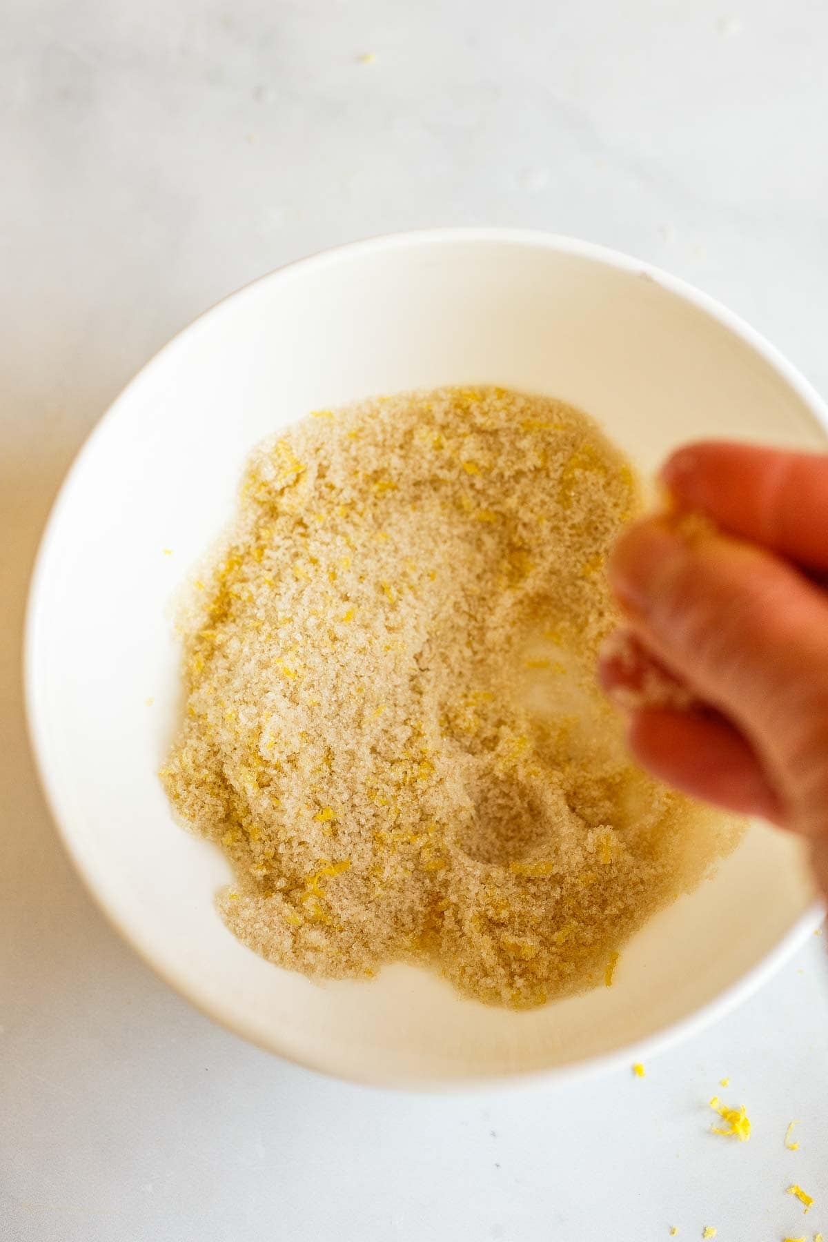 hand rubbing lemon zest into a bowl of sugar.