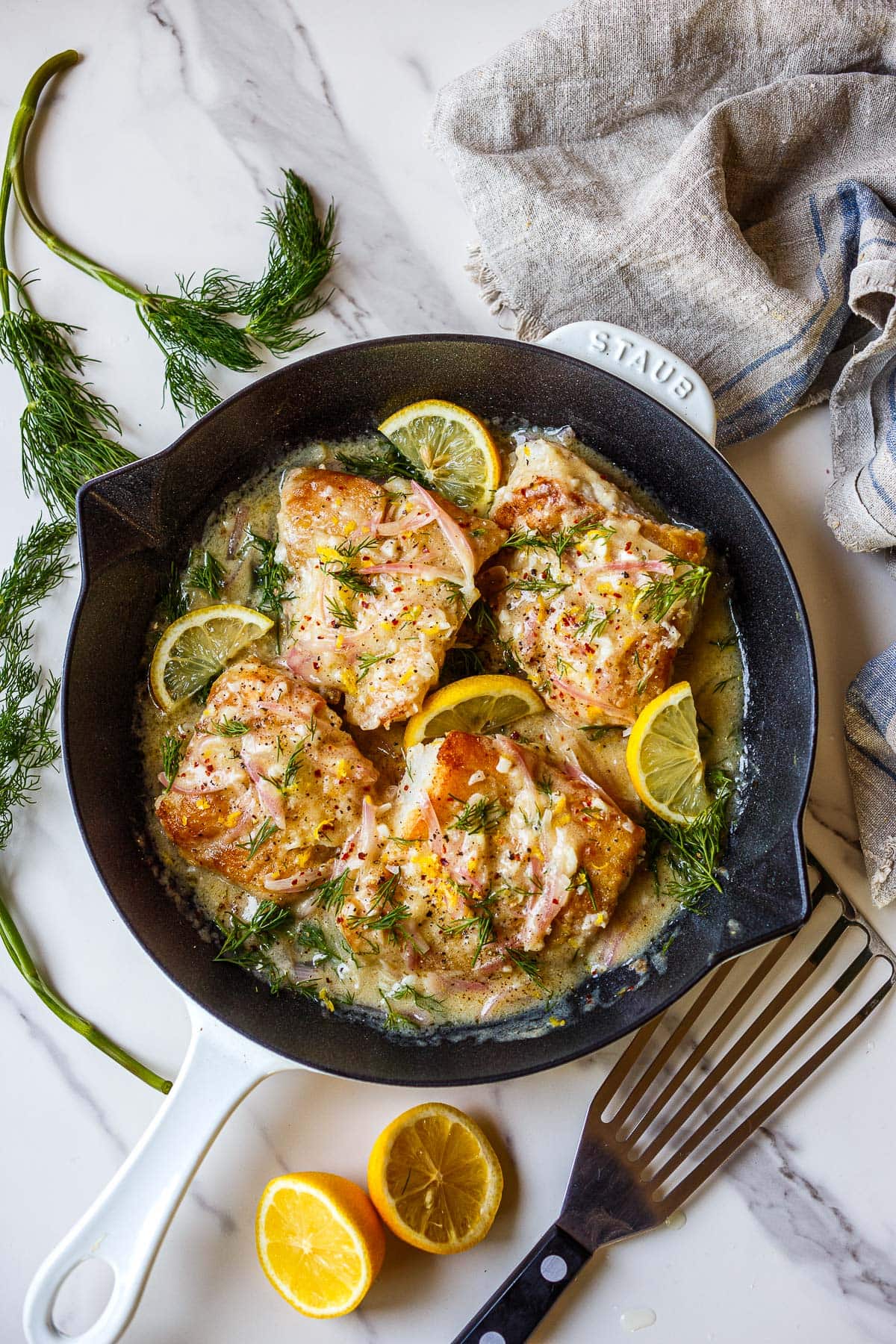 lemon butter cod in a skillet with lemon, dill, and shallots.