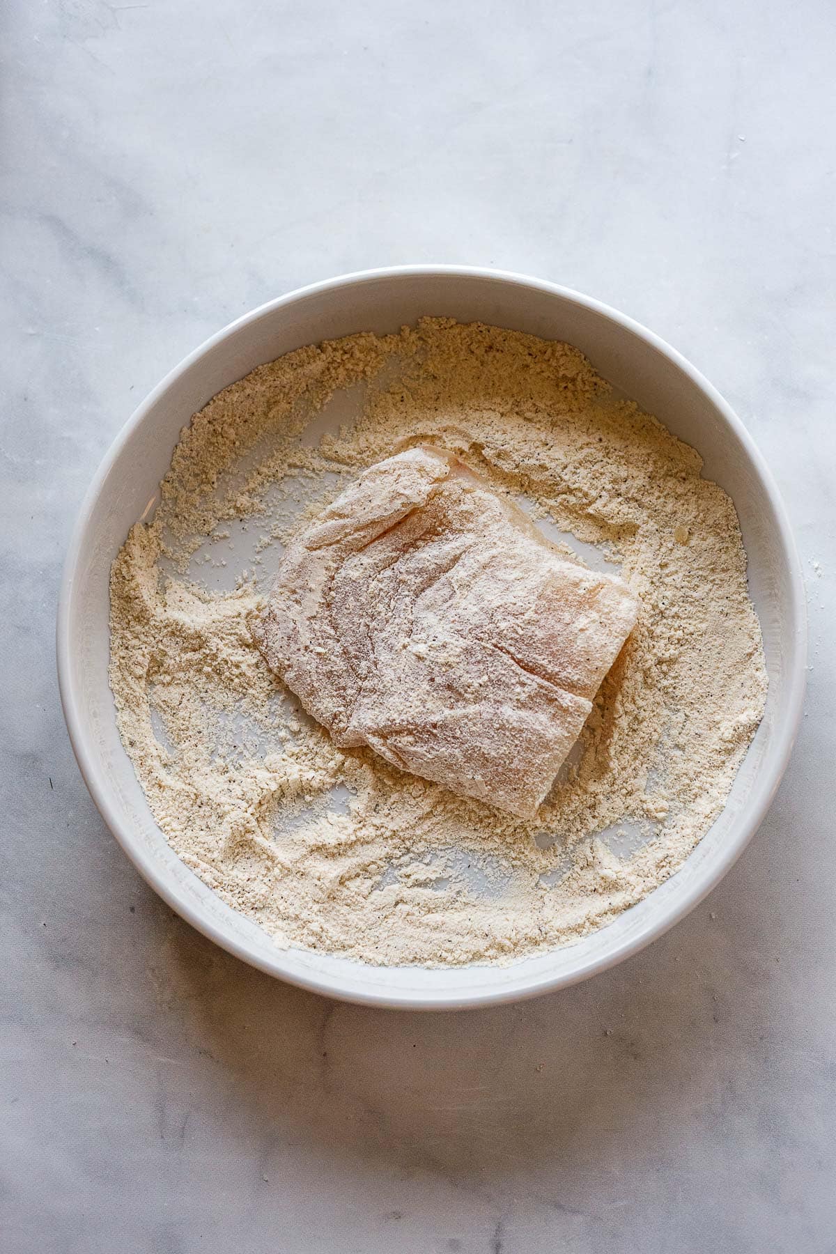 cod fillet dredged in flour in a plate.