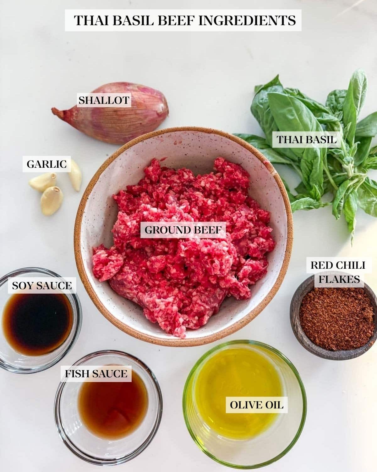 ingredients for basil beef - shallot, fresh basil, garlic cloves, ground beef, chili flakes, olive oil, fish sauce, and soy sauce, arranged neatly in bowls.