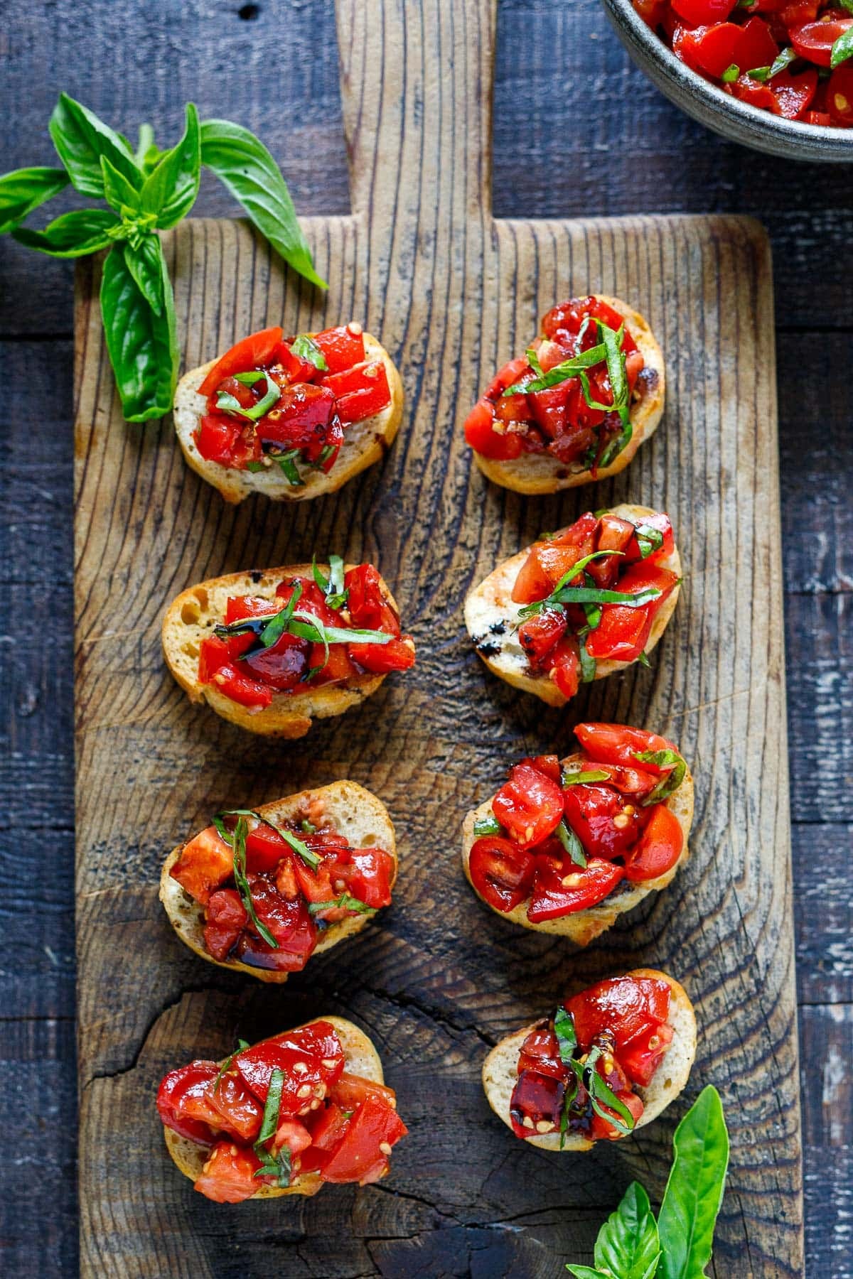 tomato bruschetta on a cutting board with basil and balsamic glaze