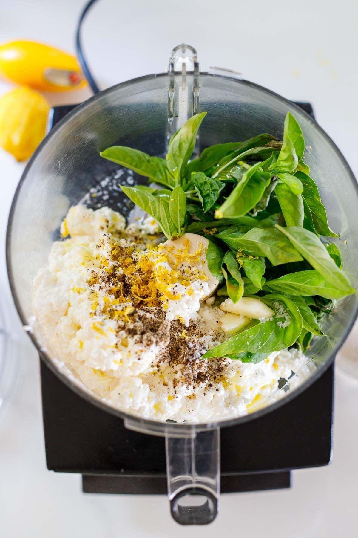 ingredients for whipped cottage cheese dip in a food processor - basil, cottage cheese, lemon zest, salt, pepper, garlic cloves.