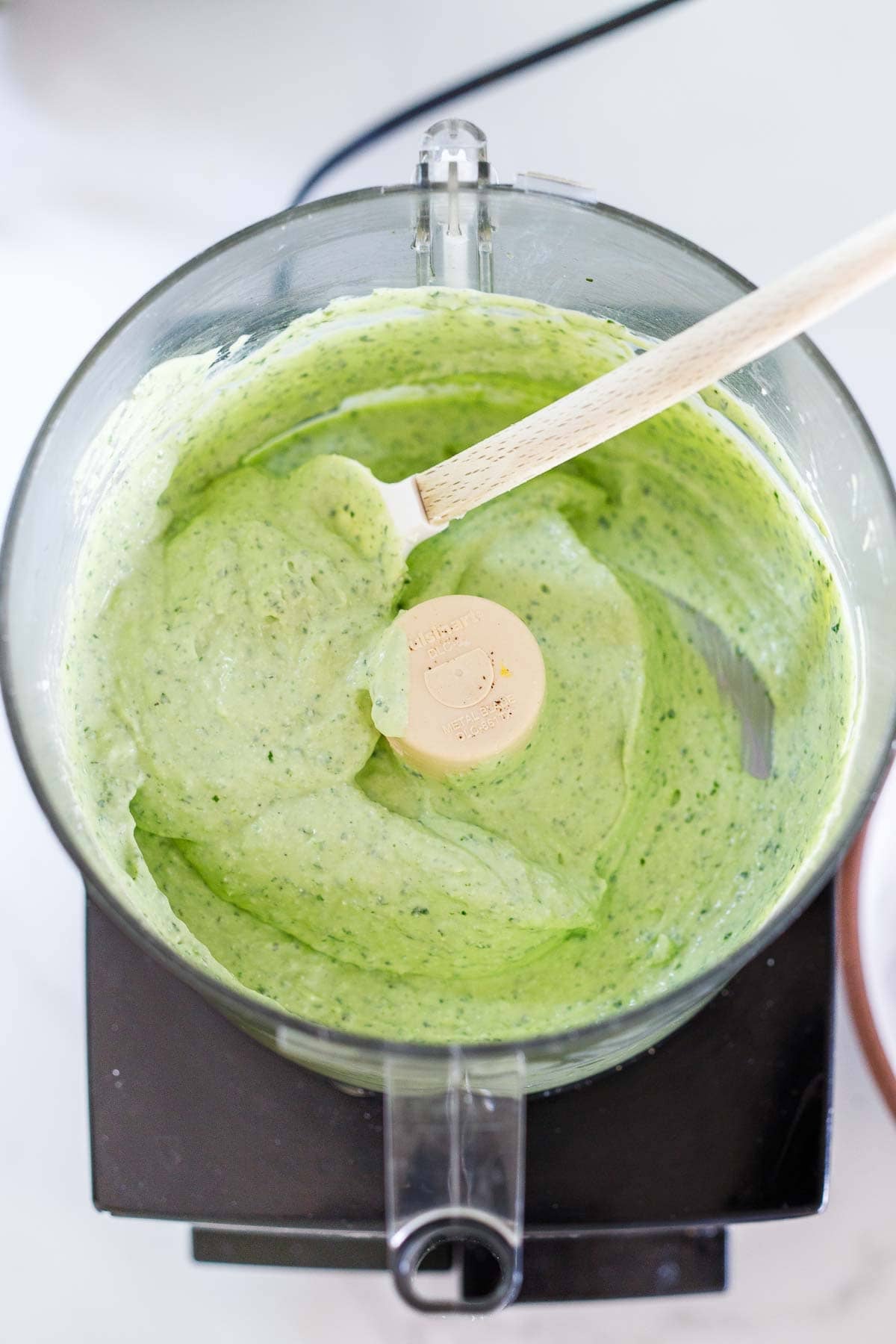 creamy whipped cottage cheese dip and spatula in a food processor with a vibrant green color from the basil.