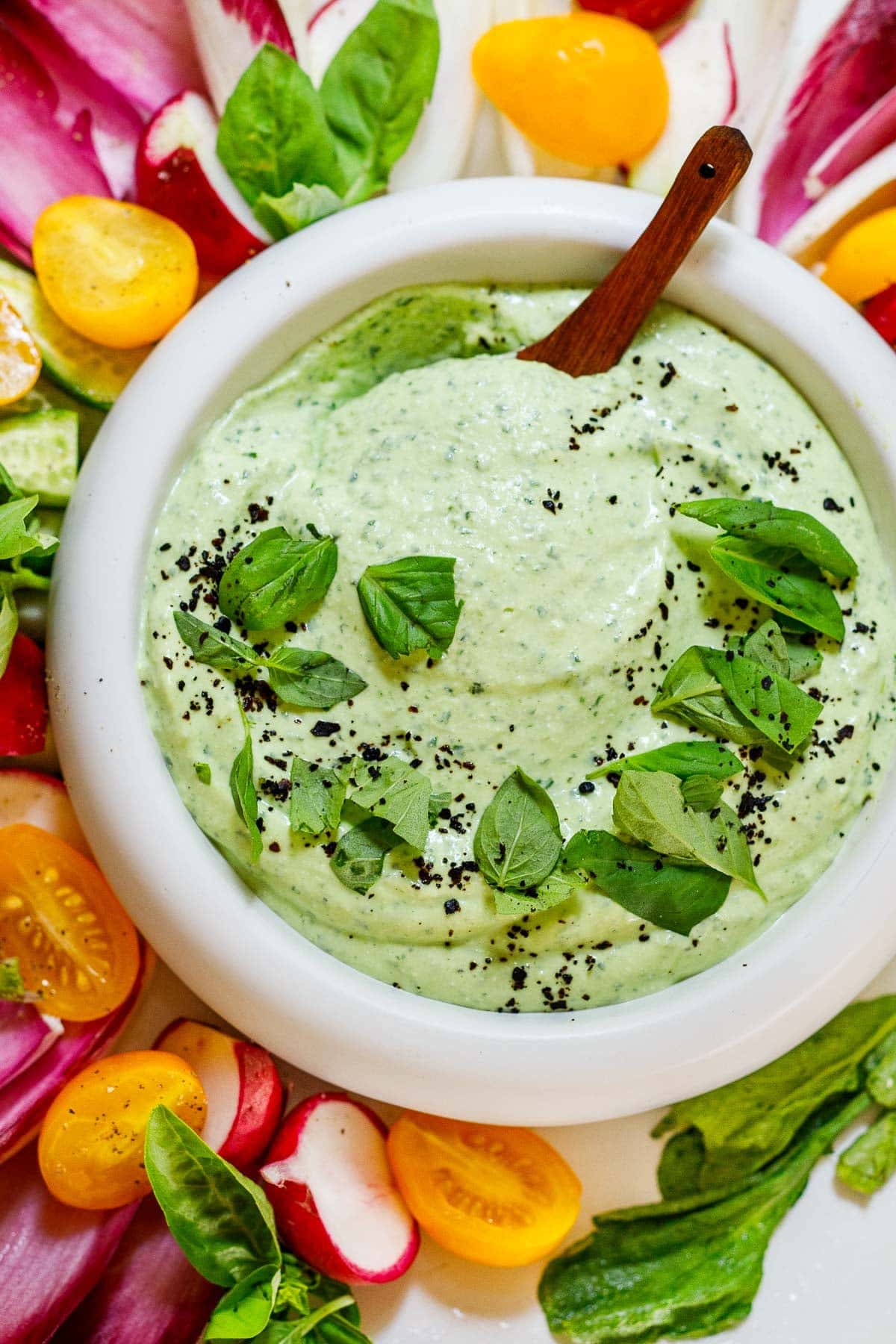 whipped cottage cheese dip with basil and urfa biber, with a wood spoon, surrounded by colorful, crisp veggies.