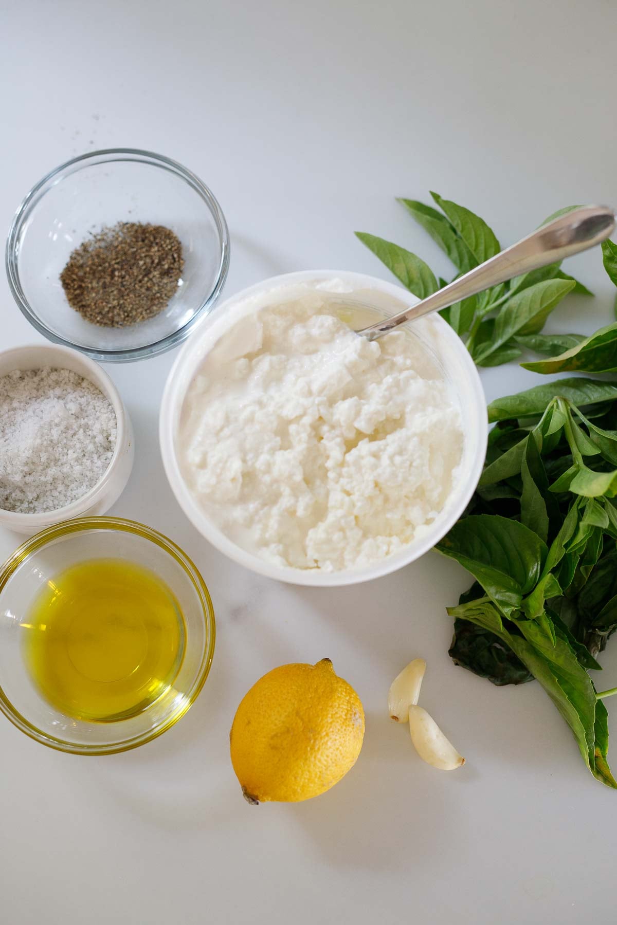 ingredients for whipped cottage cheese dip - bowl of cottage cheese, fresh basil, small bowls of salt, pepper, and olive oil, lemon, garlic cloves.