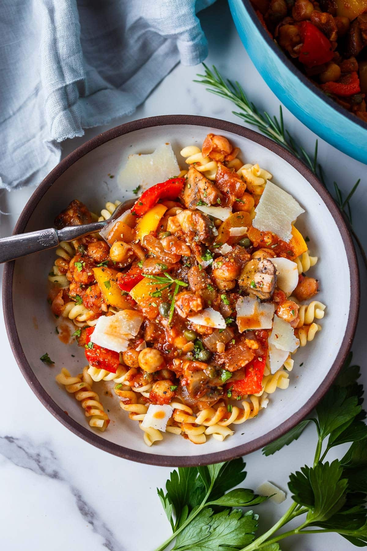 vegetarian chickpea cacciatore served over pasta with shaved pecorino romano in a bowl with a silver fork.