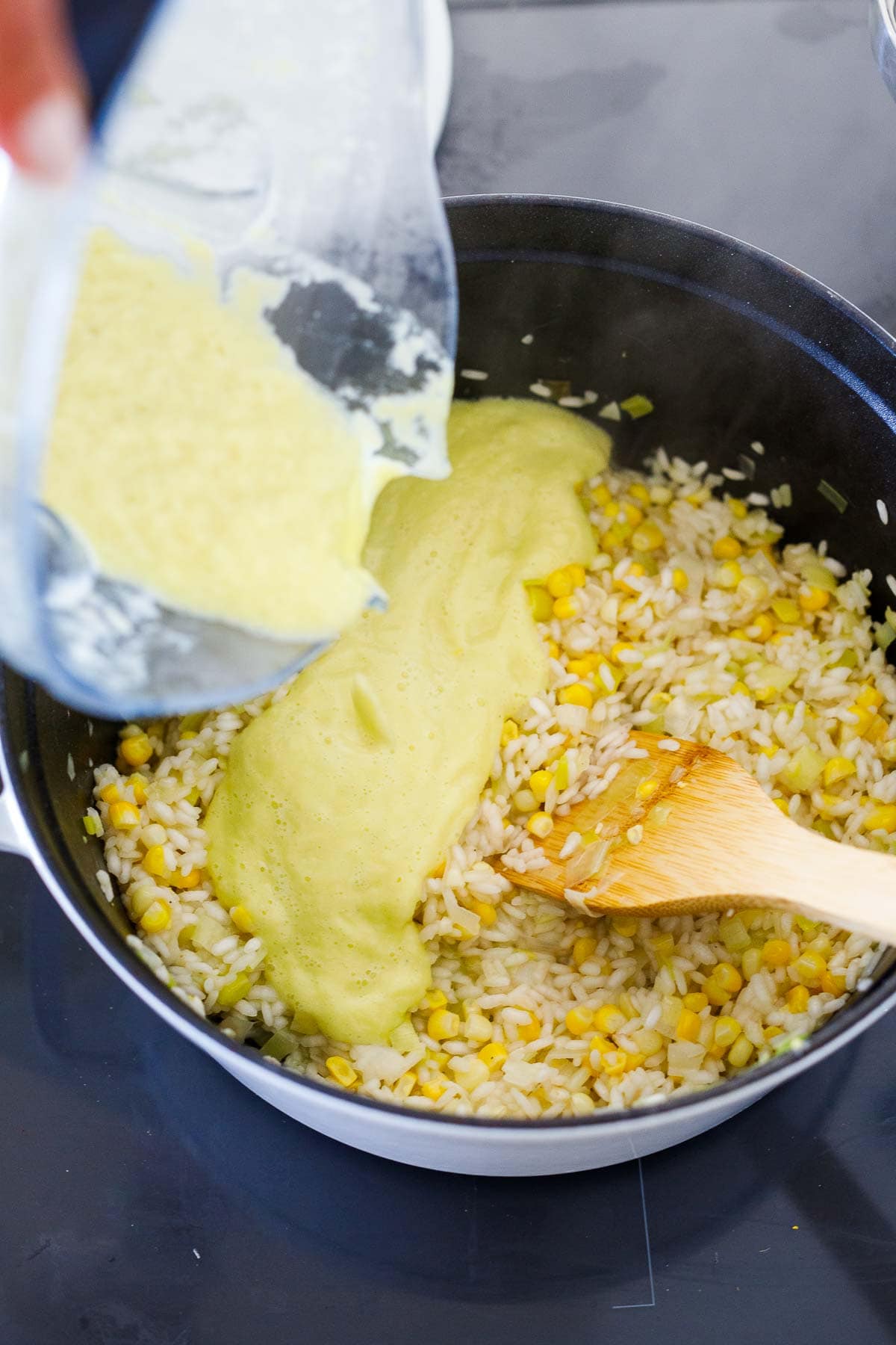 pouring corn leek purée from blender into the pot of corn risotto.