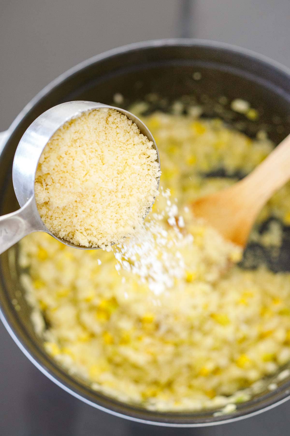 pouring a measuring cup of Parmesan into a pot of corn risotto.
