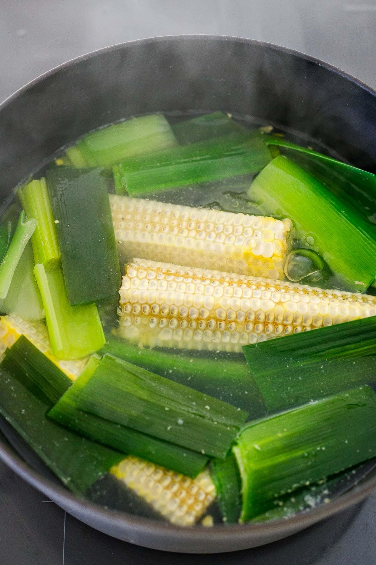 soup pot with shaved ears of corn and green tops of leeks in water to make broth.