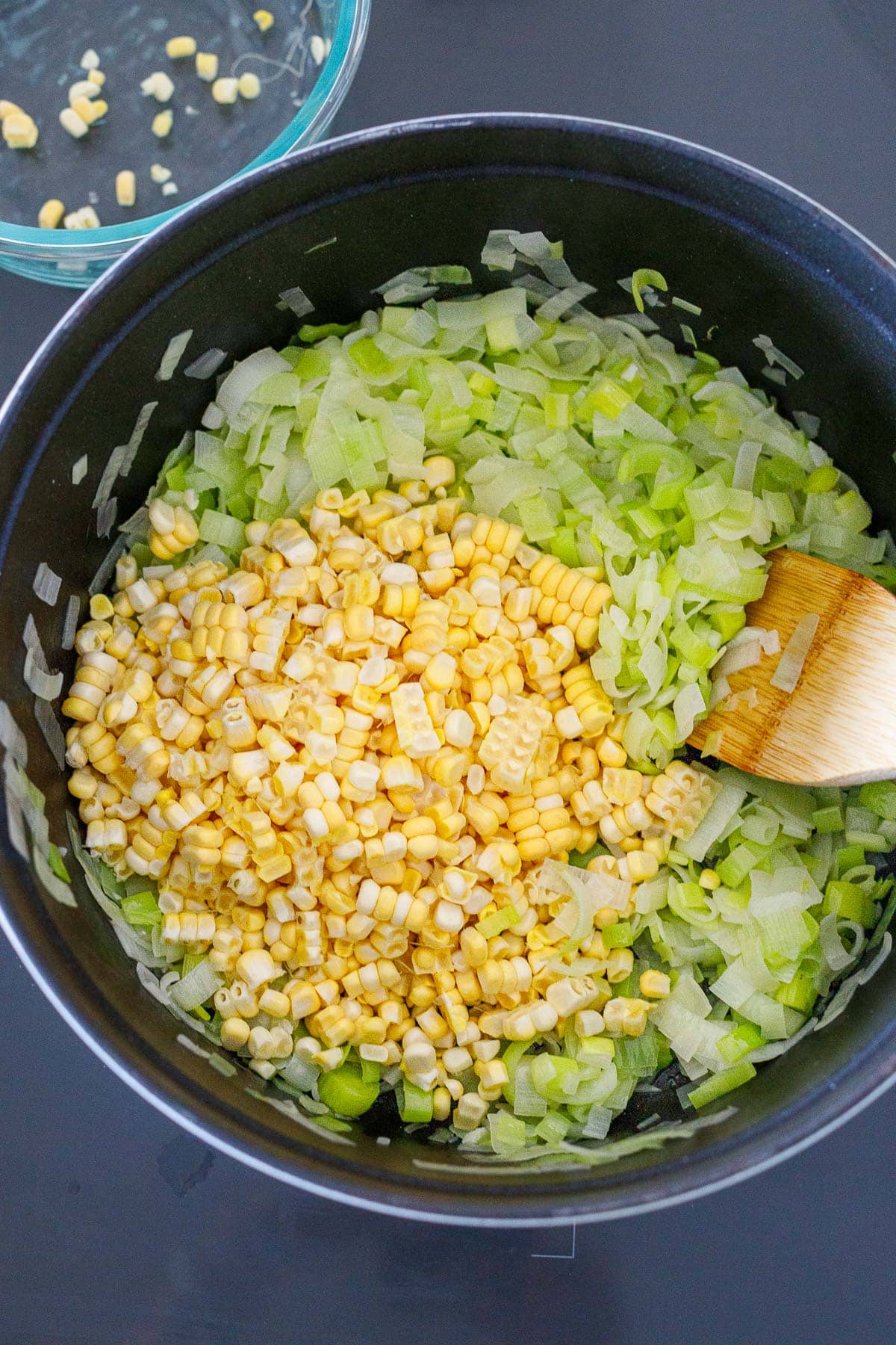 pot with shaved corn kernels and sautéed leeks with wooden spatula.