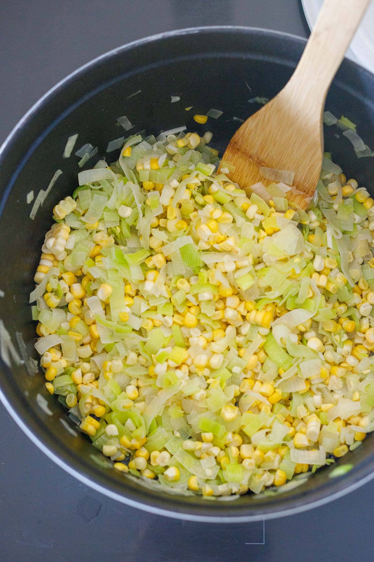 pot with sautéed leeks and corn to make corn risotto with a wood spatula.
