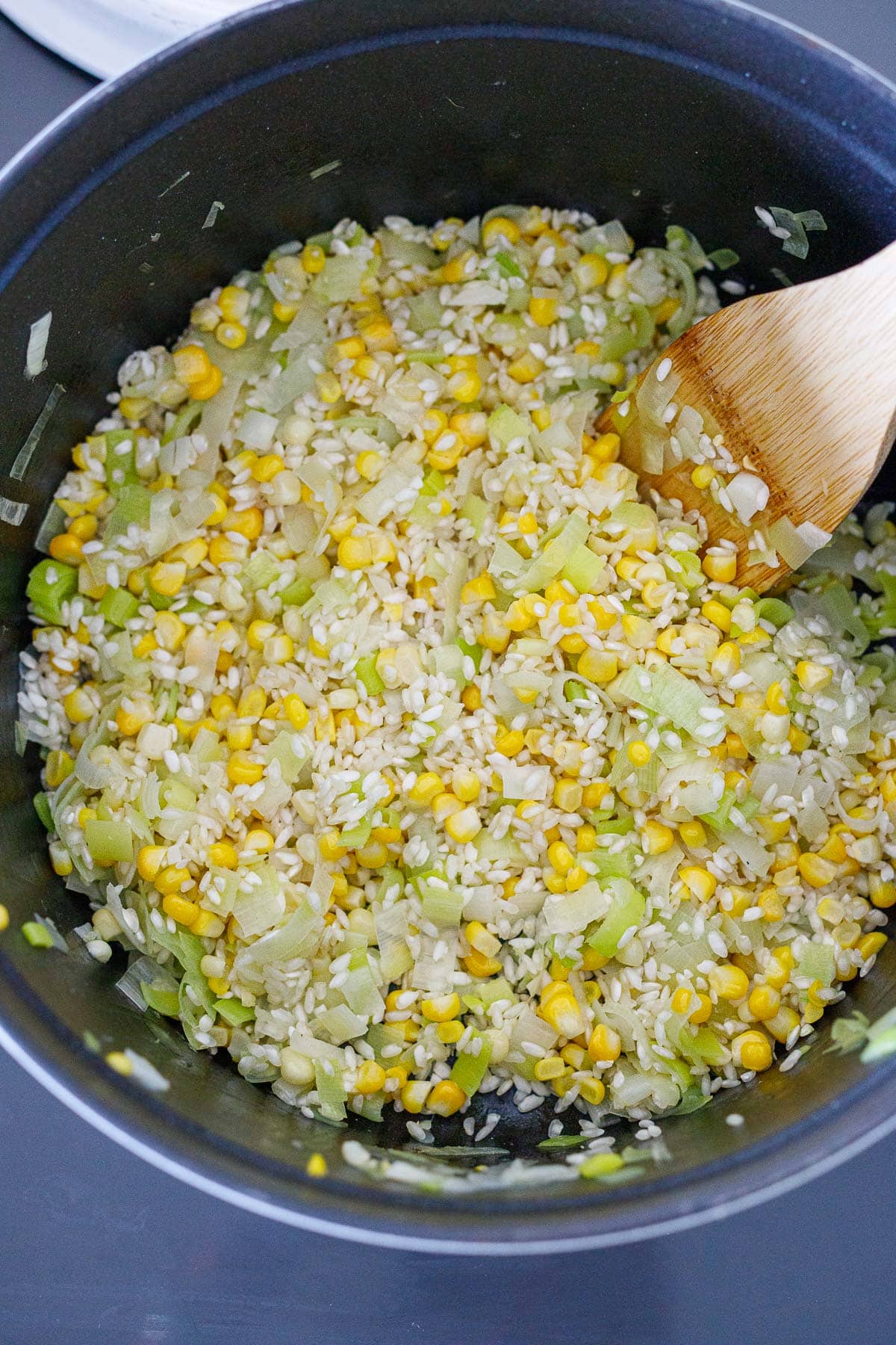pot with corn kernels, leeks, and arborio rice with a wooden spatula to make corn risotto.