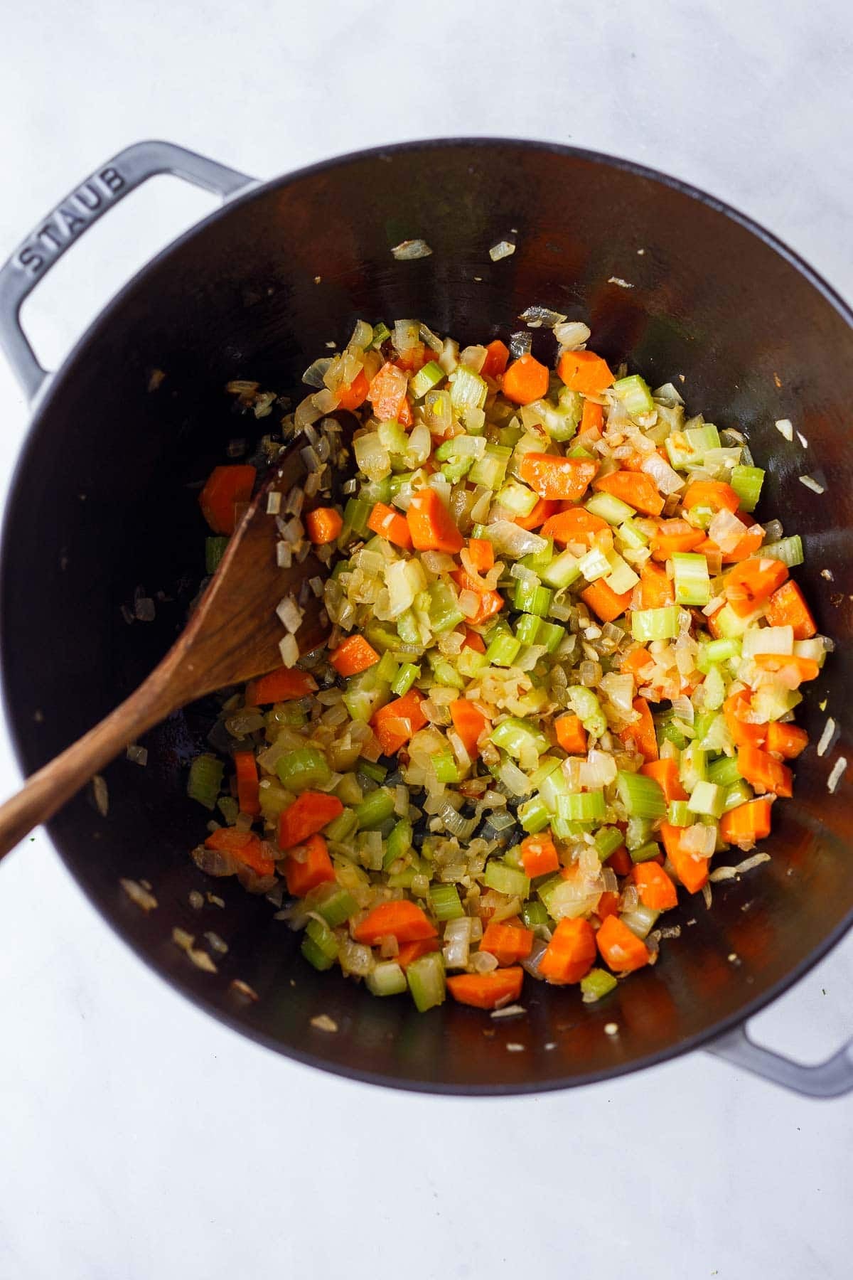 dutch oven with sautéed carrots, onion, and celery, with a wood spoon, prepping to make creamy chicken noodle soup.
