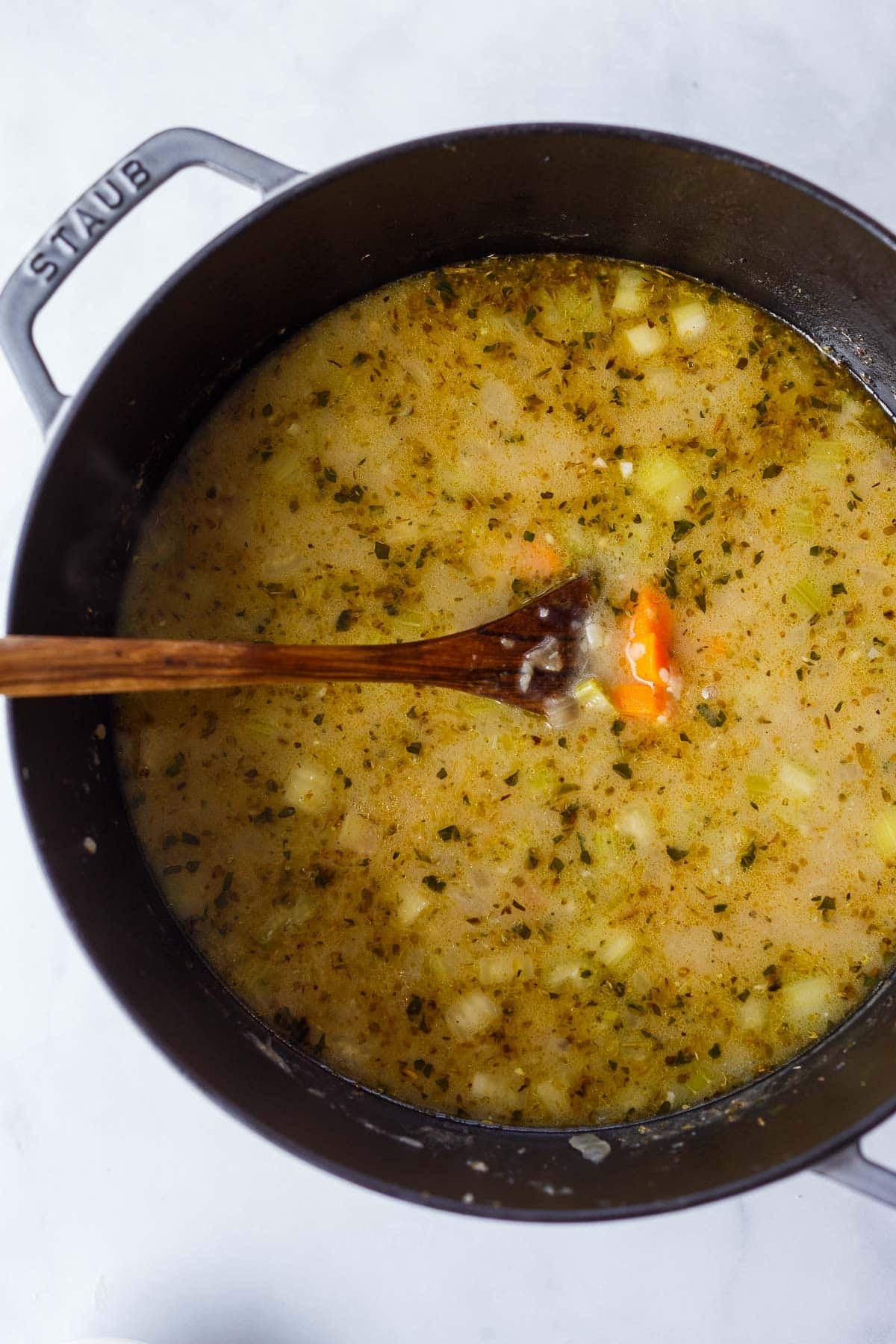 chicken broth and veggies in a dutch oven with a wooden spoon, making creamy chicken noodle soup.