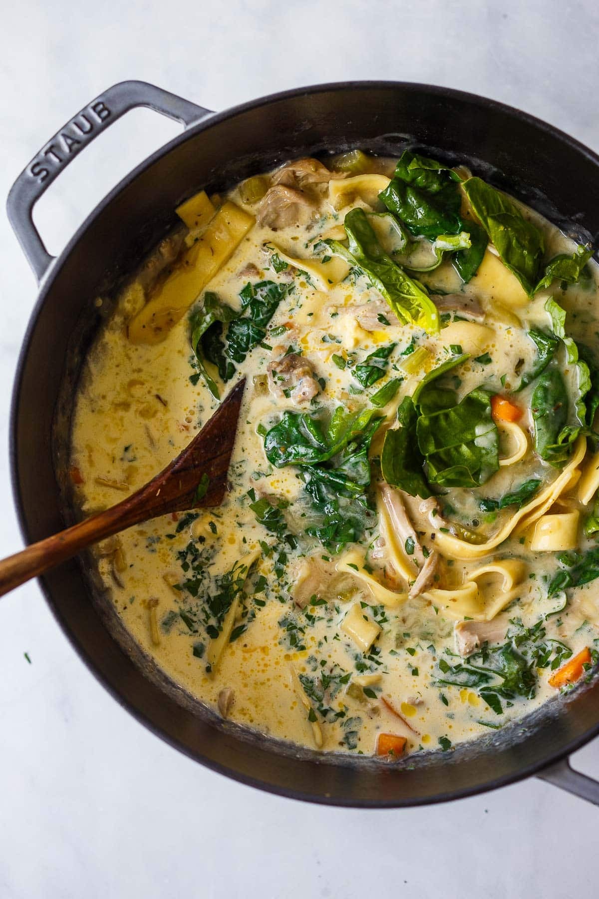 dutch oven with creamy chicken noodle soup with fresh spinach added to the pot.