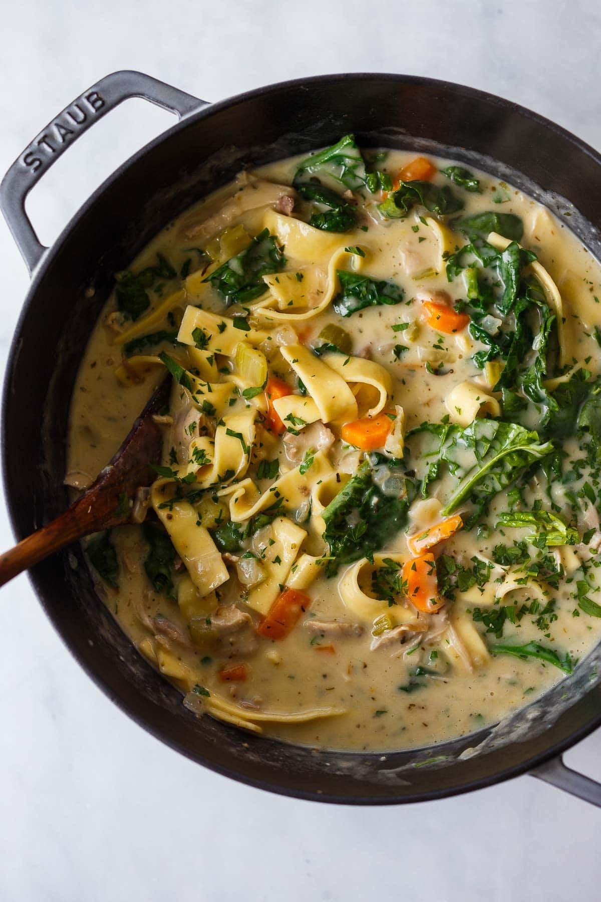cooking creamy chicken noodle soup with spinach in a large dutch oven with a wooden spoon to stir.