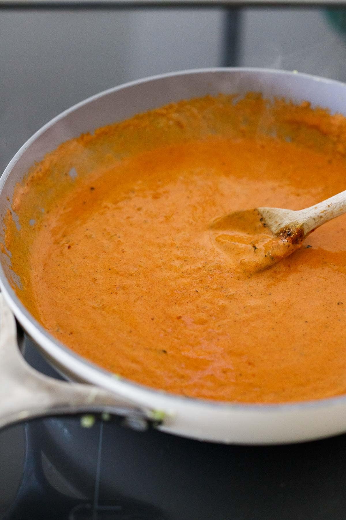 simmering creamy tikka masala sauce in a skillet with a wooden spoon.