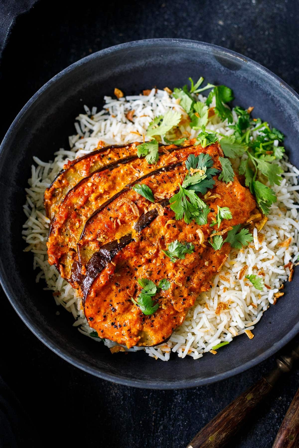 baked eggplant tikka masala slices on basmati rice with fresh cilantro and crispy shallots.