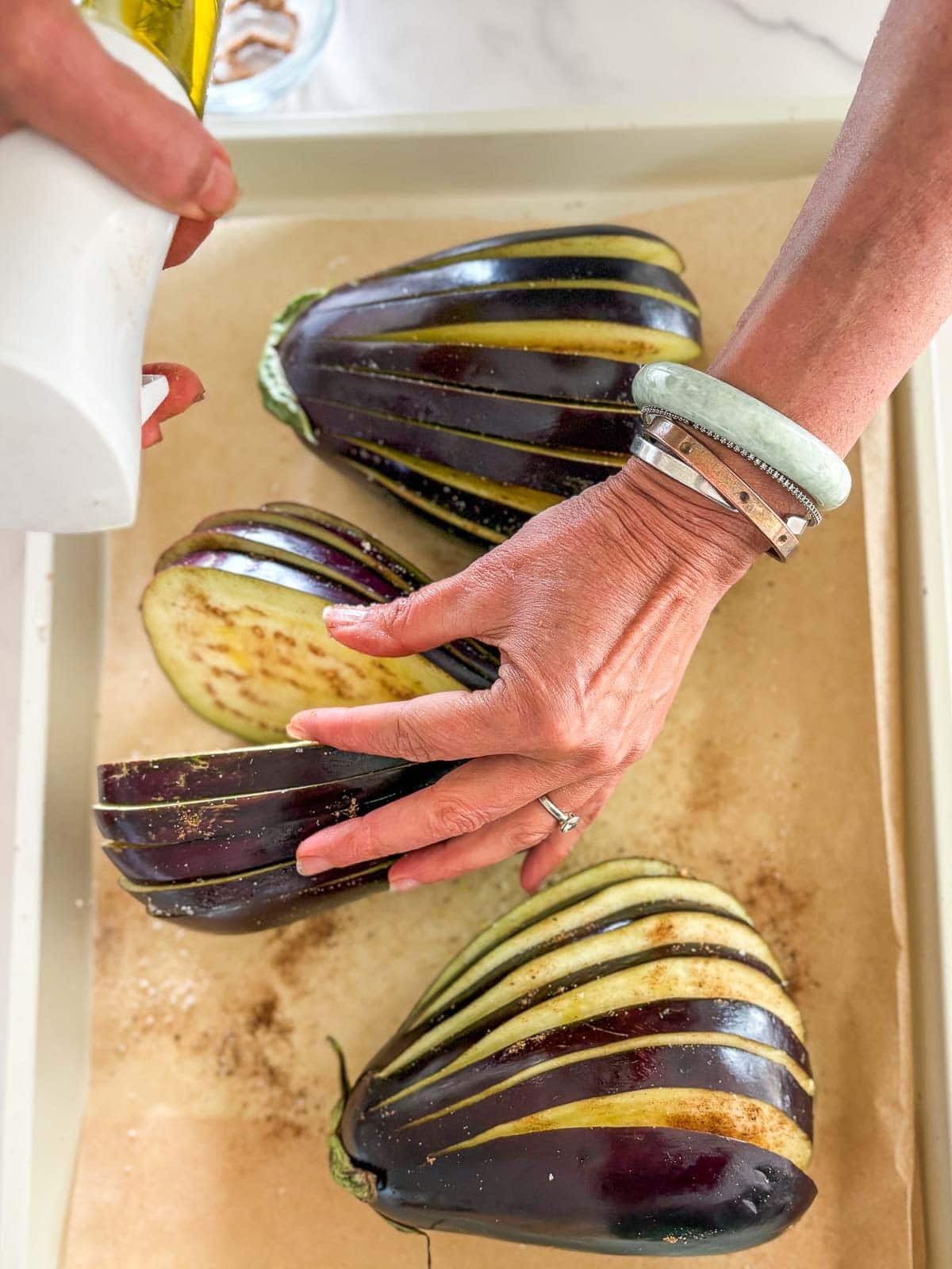 spraying olive oil in between the eggplant slices on a parchment-lined baking sheet.