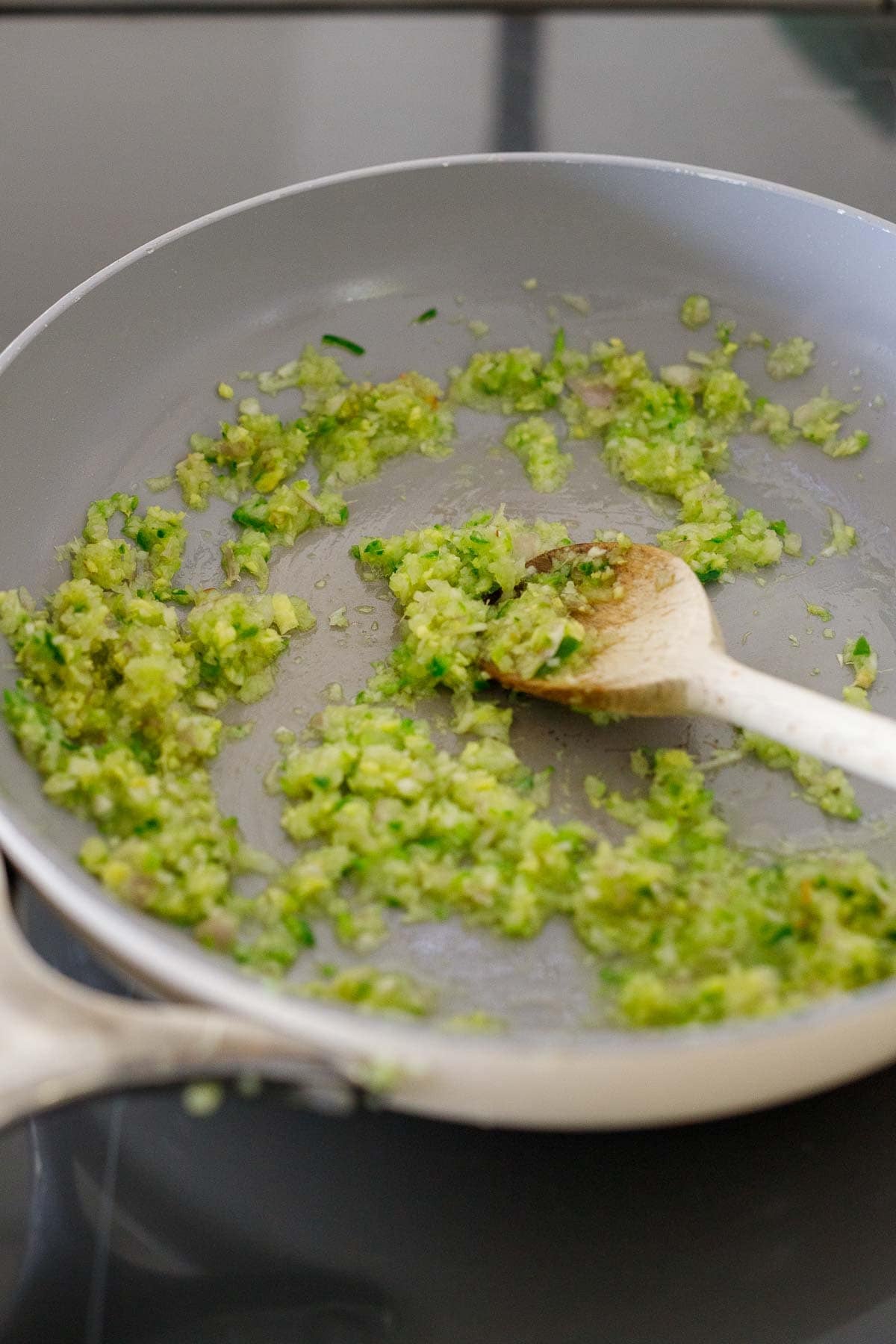 serrano chili mixture sautéing in a skillet with a wooden spoon.
