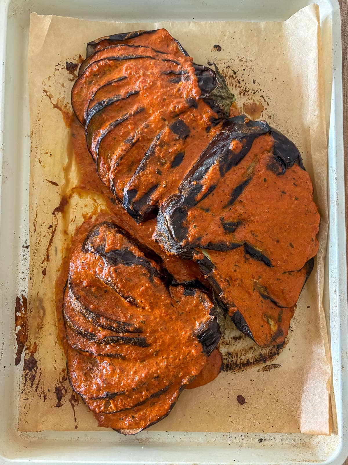 baked eggplant slices in creamy tikka masala sauce on a parchment-lined sheet pan.