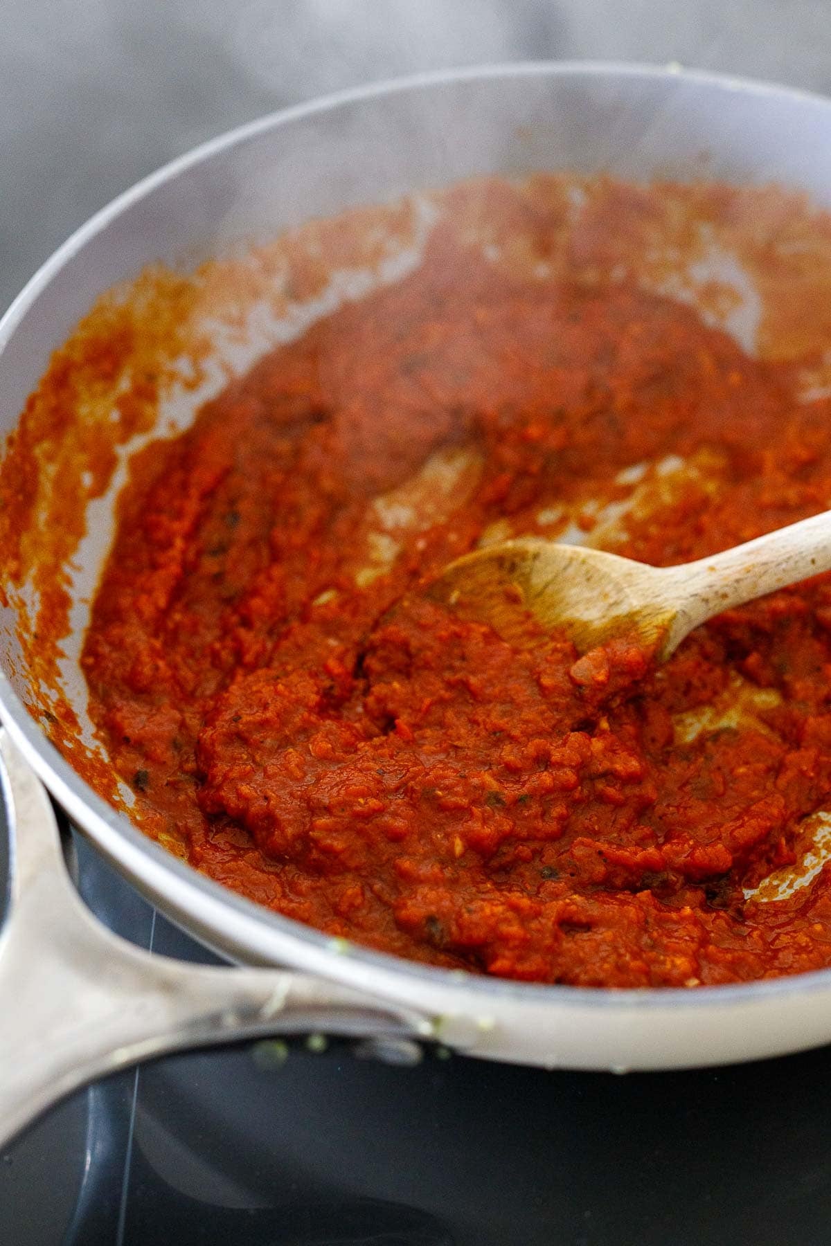 simmering tomato tikka masala sauce in a skillet with a wooden spoon.