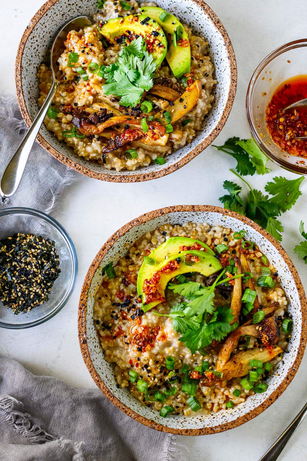 two bowls of savory oats with avocado, sautéed mushrooms, cilantro, and chili crisp.