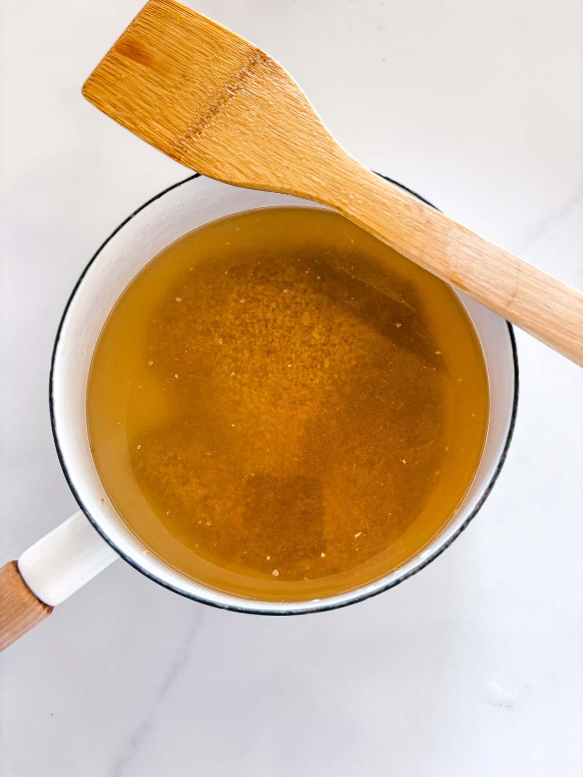 saucepan with steel cut oats and broth, with a wooden spatula resting on the edge.
