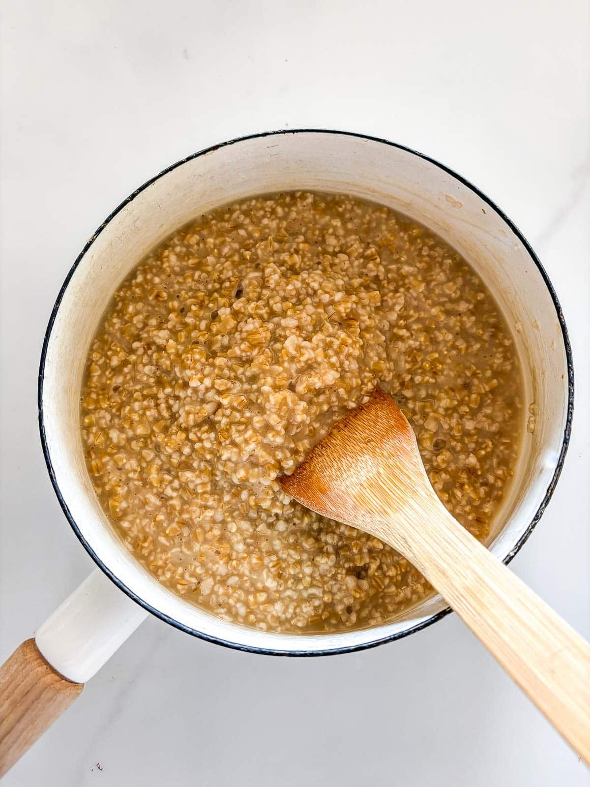 cooked steel cut oats in a saucepan with a wooden spatula.