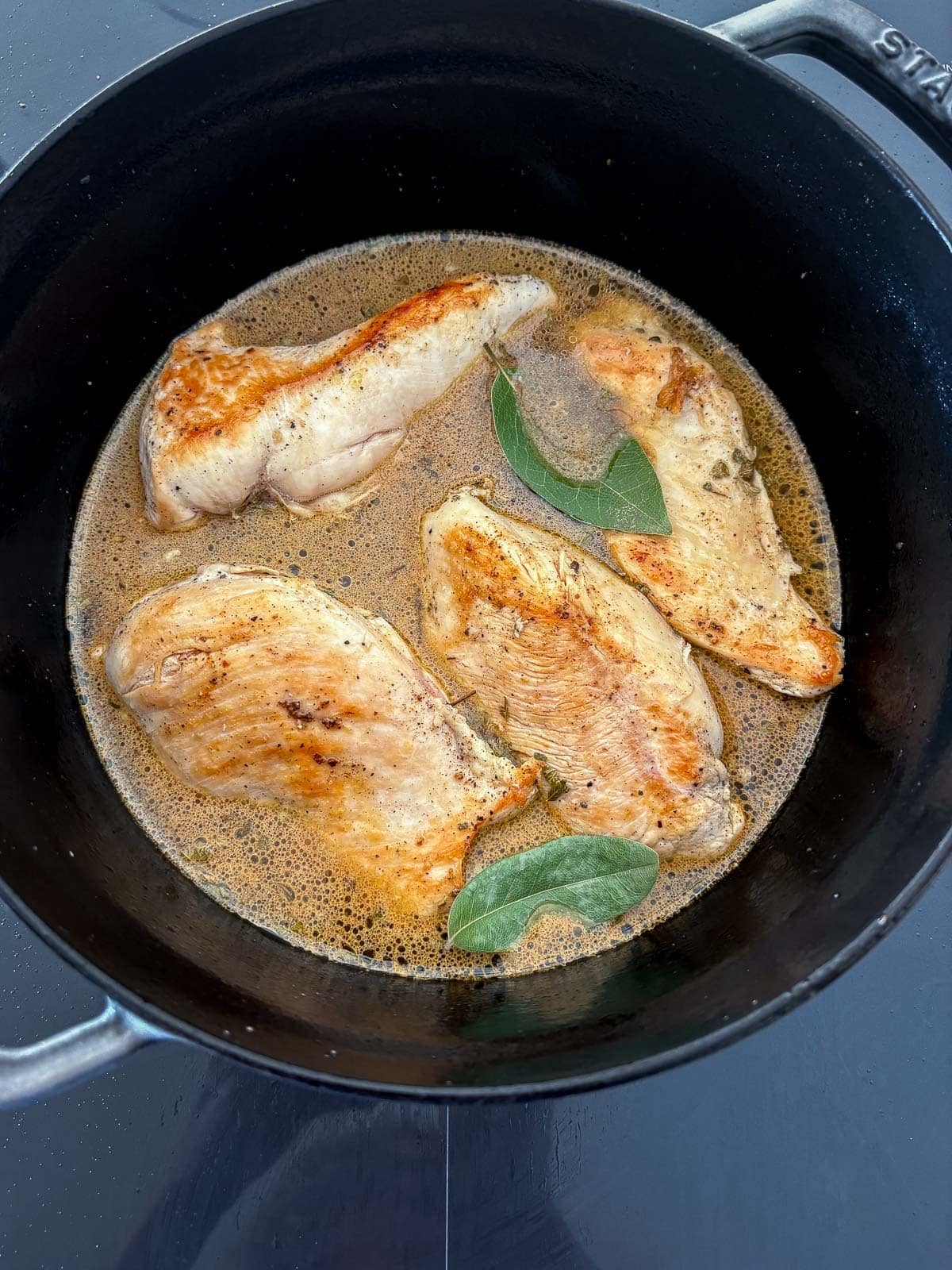 seared chicken in cooking liquid with bay leaves.