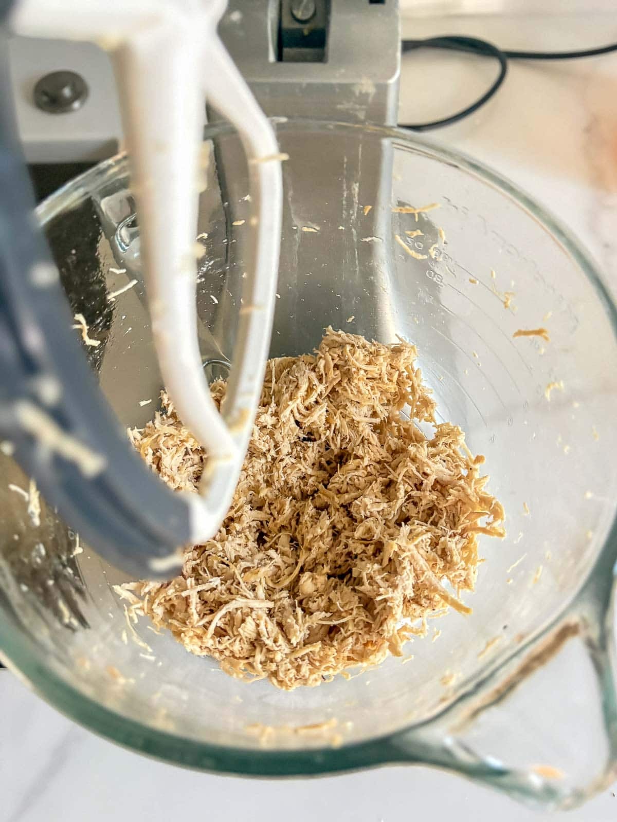 shredded chicken in a mixing bowl with a paddle attachment.
