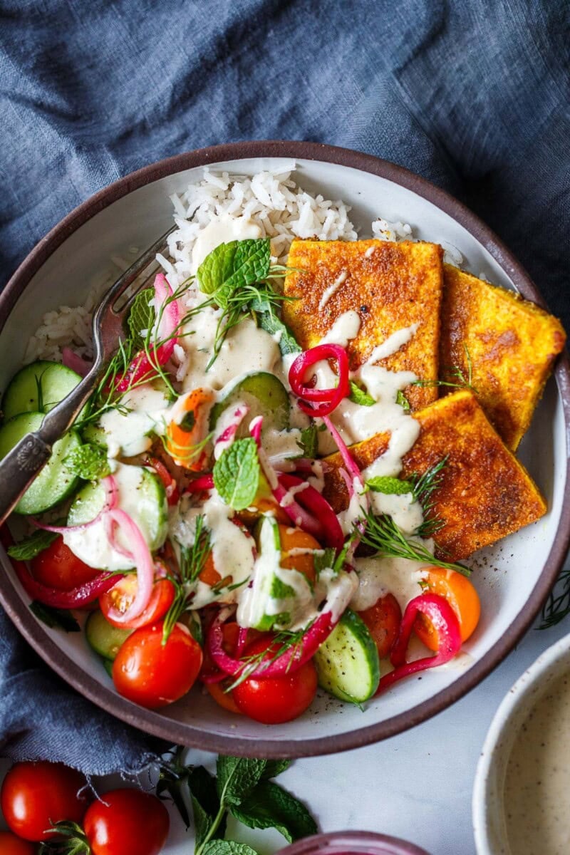 Then comes the best part - the sauce! Drizzle generously with creamy tahini sauce, tzatziki, or zhoug to bring it all together.