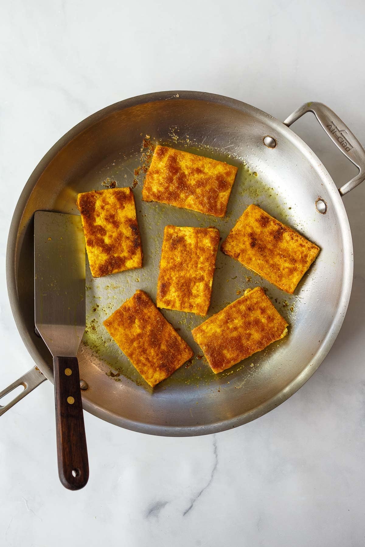 shawarma tofu slabs searing in a skillet with a spatula.