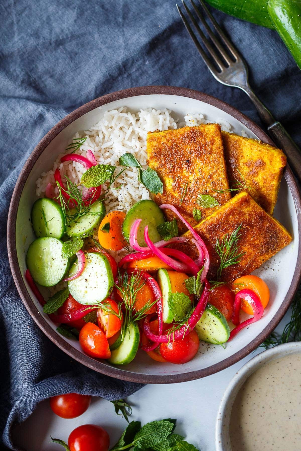 tofu shawarma bowl with rice, three seared tofu slabs, cucumber, pickled onions, tomatoes, and herbs.