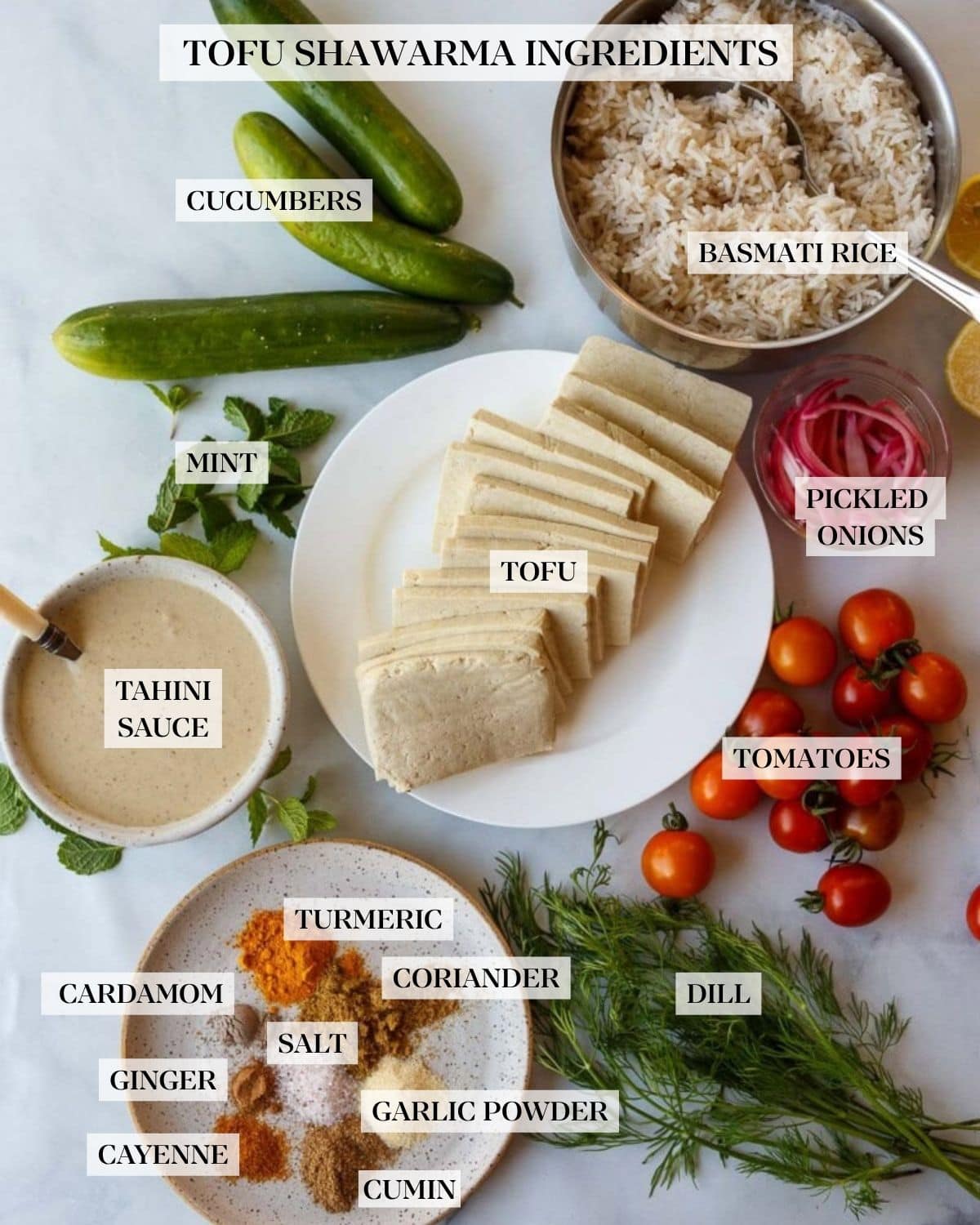 ingredients for tofu shawarma bowl laid out - three cucumbers, small pot of cooked basmati rice, small bowl of pickled onions, scattered fresh mint, plate of sliced tofu, cherry tomatoes, bowl of tahini sauce, plate of shawarma spices, fresh dill bunch.