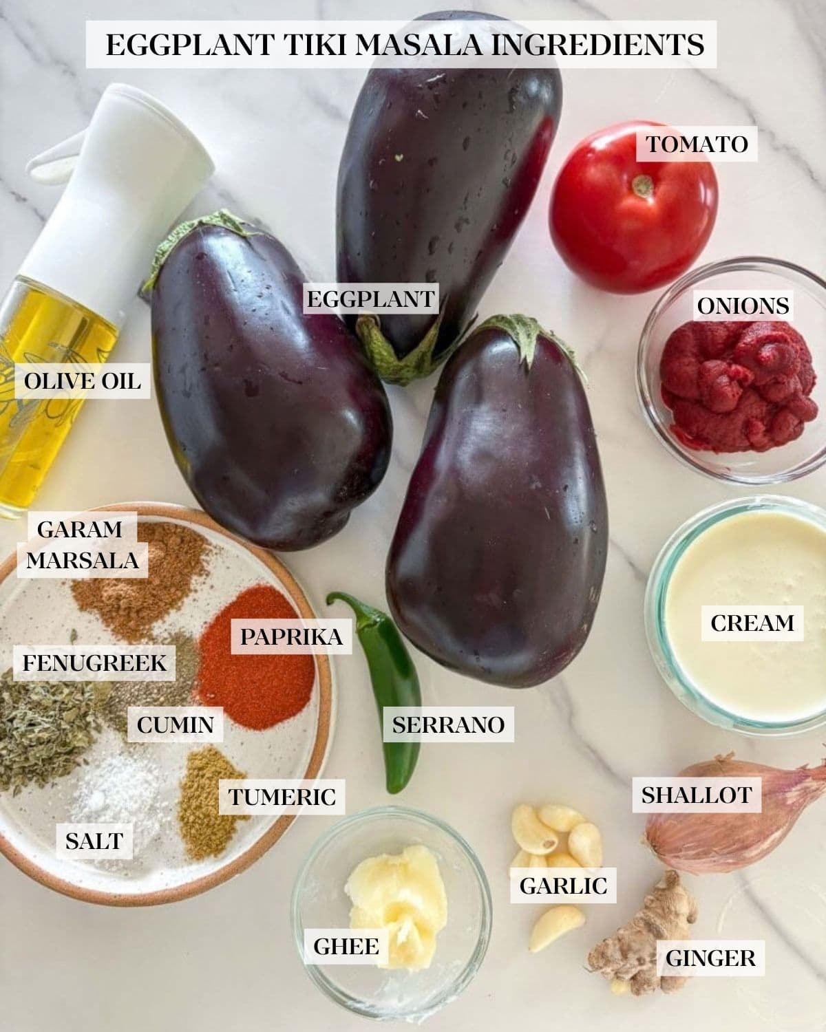 ingredients for eggplant tikka masala - three globe eggplants, tomato, glass bowl of tomato paste, glass bowl of heavy cream, shallot, fresh ginger, peeled garlic cloves, small glass bowl of ghee, serrano pepper, small plate with various spices, and a glass spray bottle with olive oil.