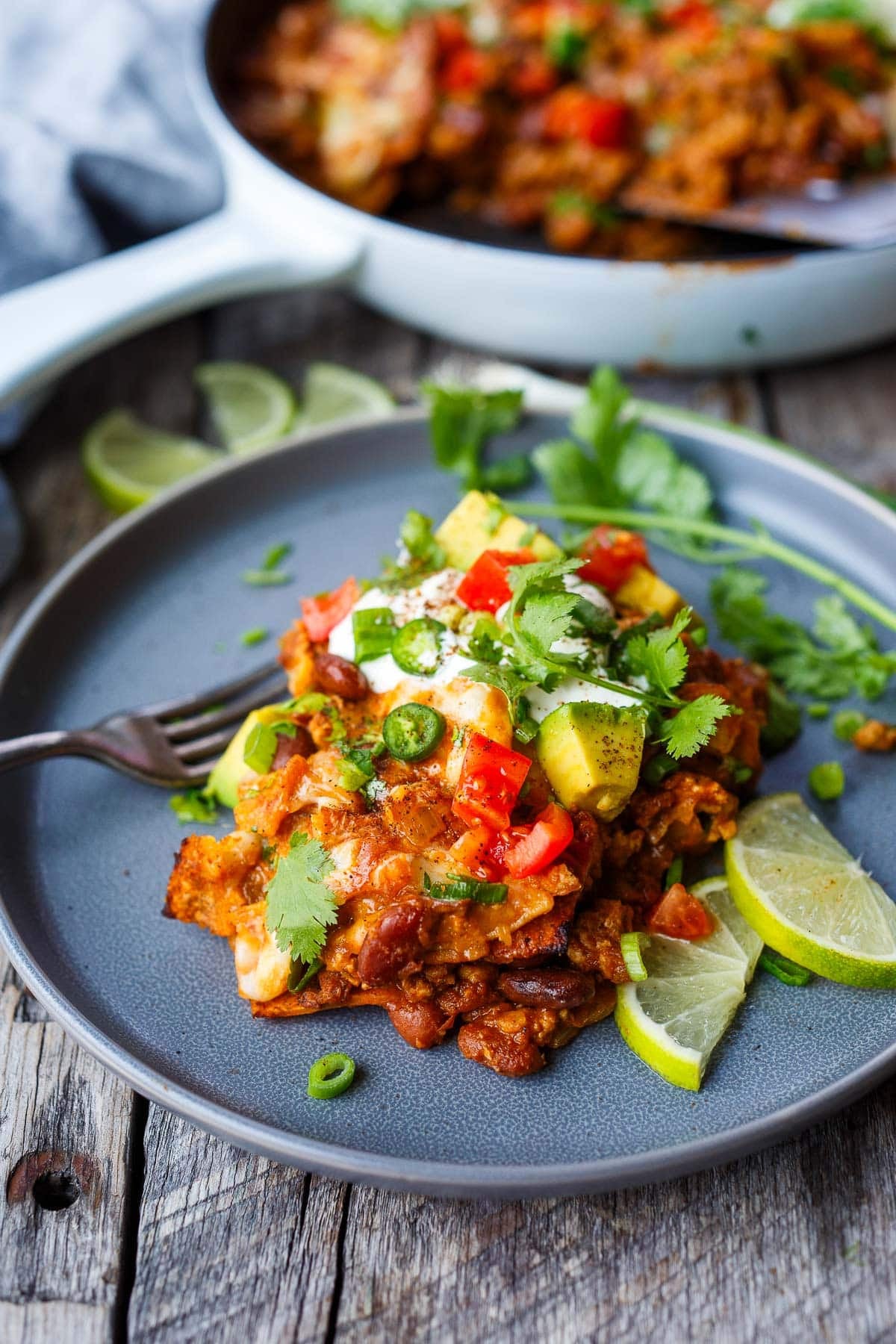 enchilada skillet served on a plate with lime wedges, cilantro, avocado, jalapeno, and fresh tomatoes.