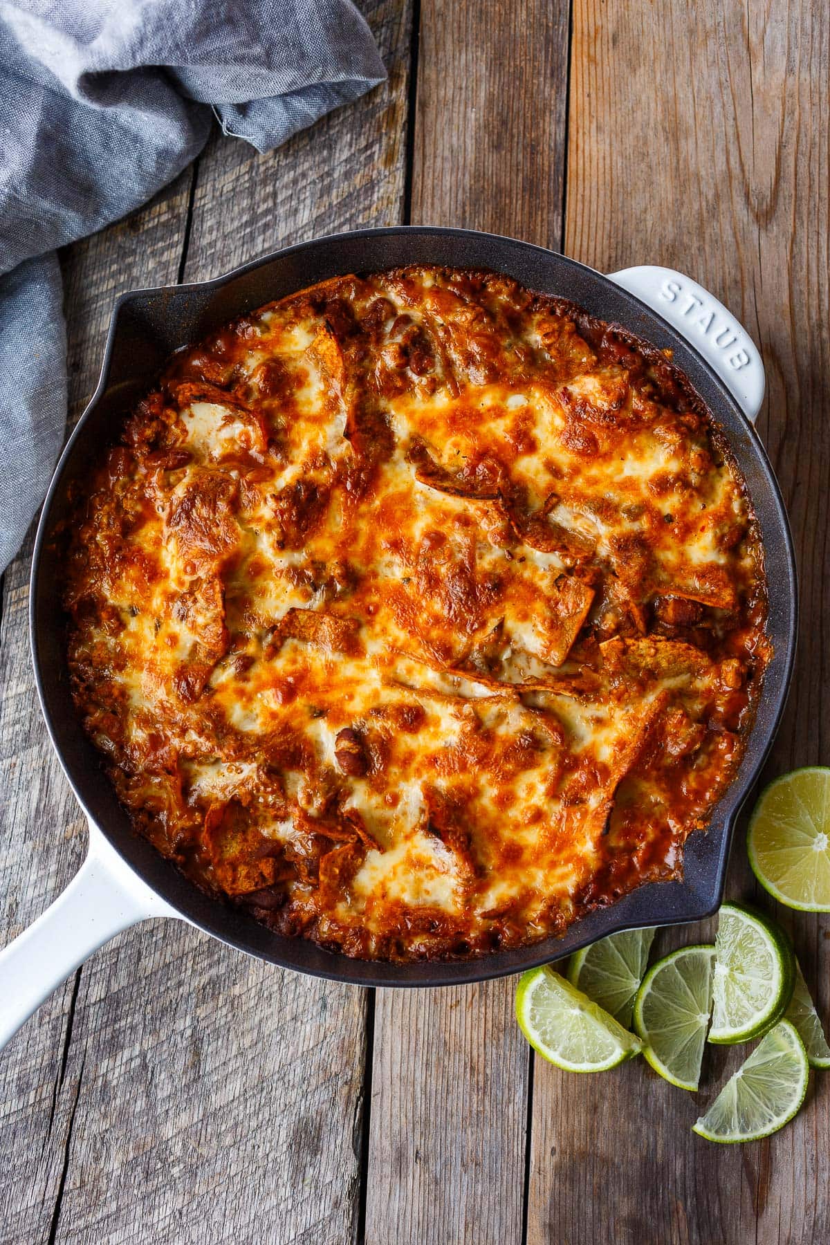 enchilada skillet with a golden cheesy topping, next to lime wedges on a wood surface.