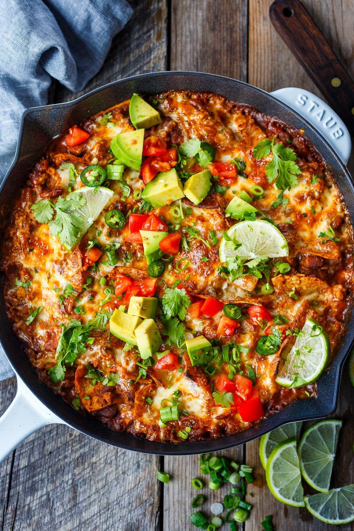 enchilada skillet with a golden cheesy topping, garnished with lime, cilantro, avocado, and tomato.