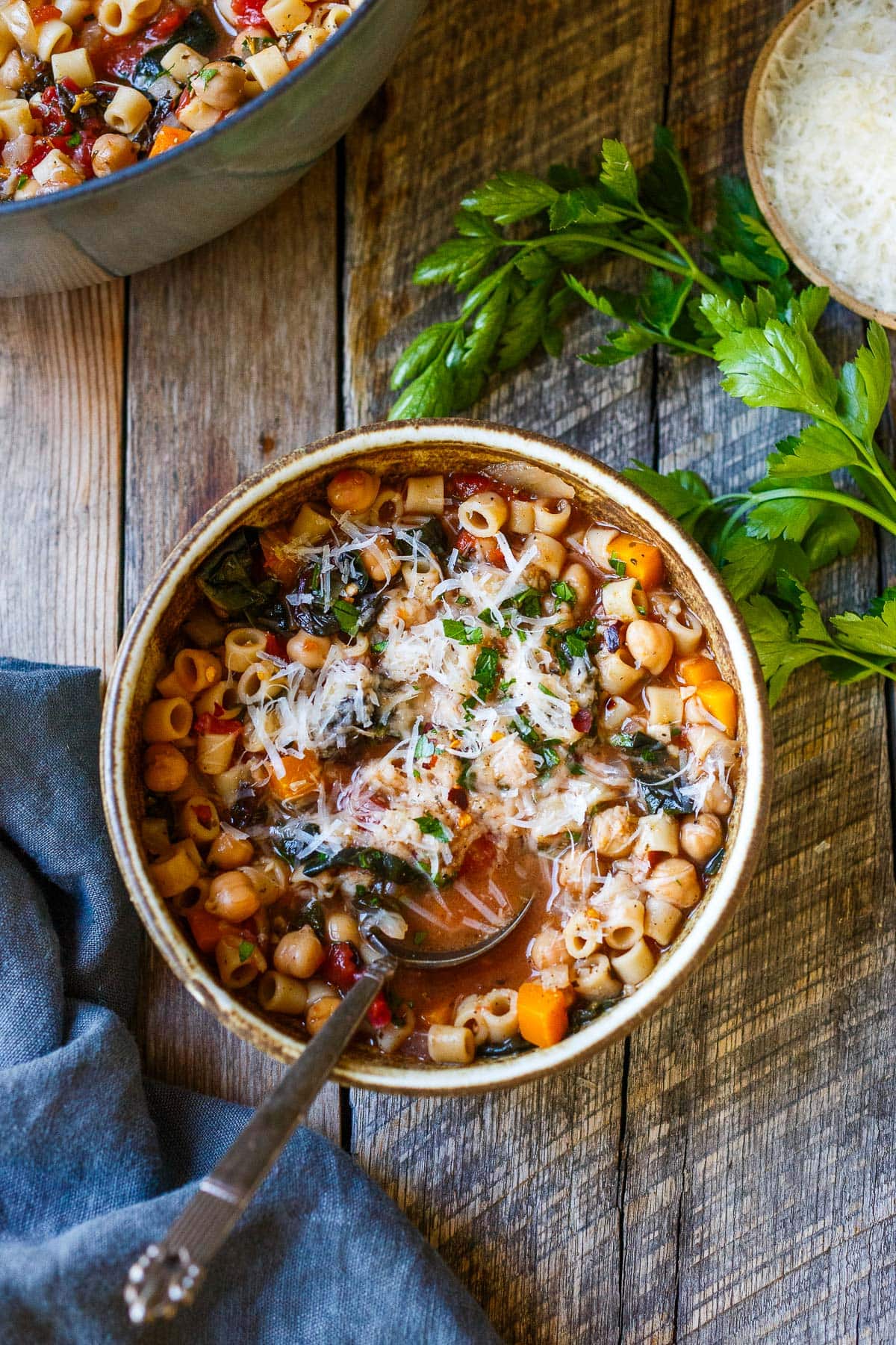 bowl of pasta e ceci with grated cheese and fresh herbs and a spoon. 