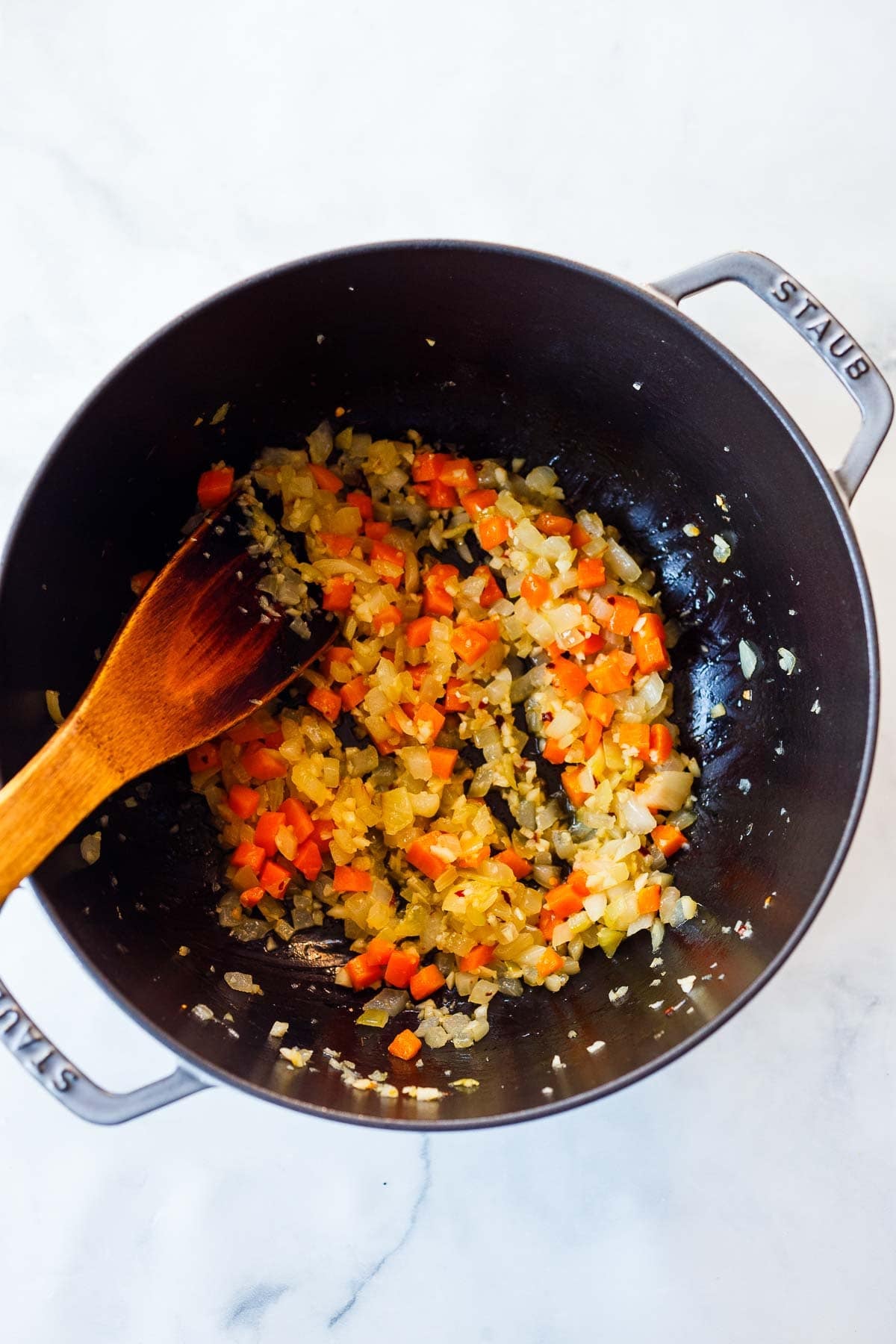 pot with sautéed onions and carrots with a wooden spatula. 